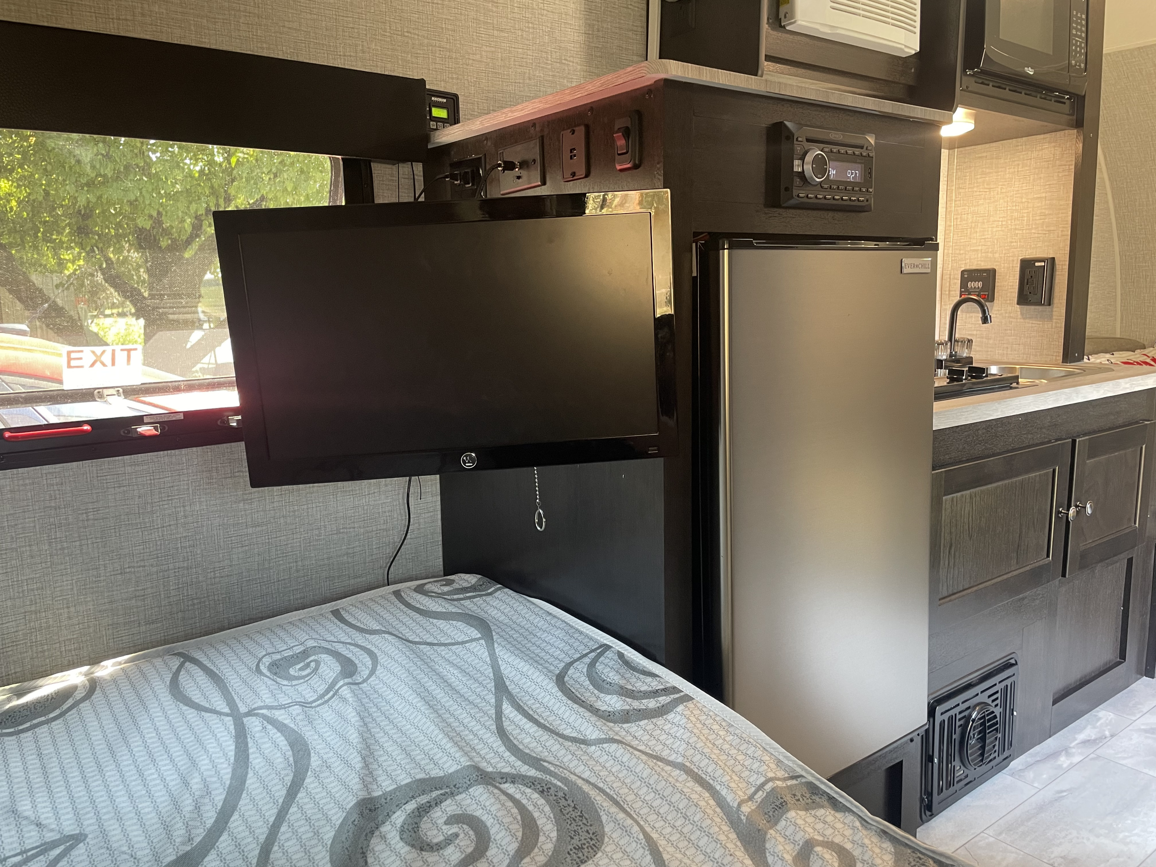 Cozy RV rental interior showing a bed, mounted TV, and compact kitchen with fridge, perfect for travel.. Braxton Creek Free Solo Plus 2022