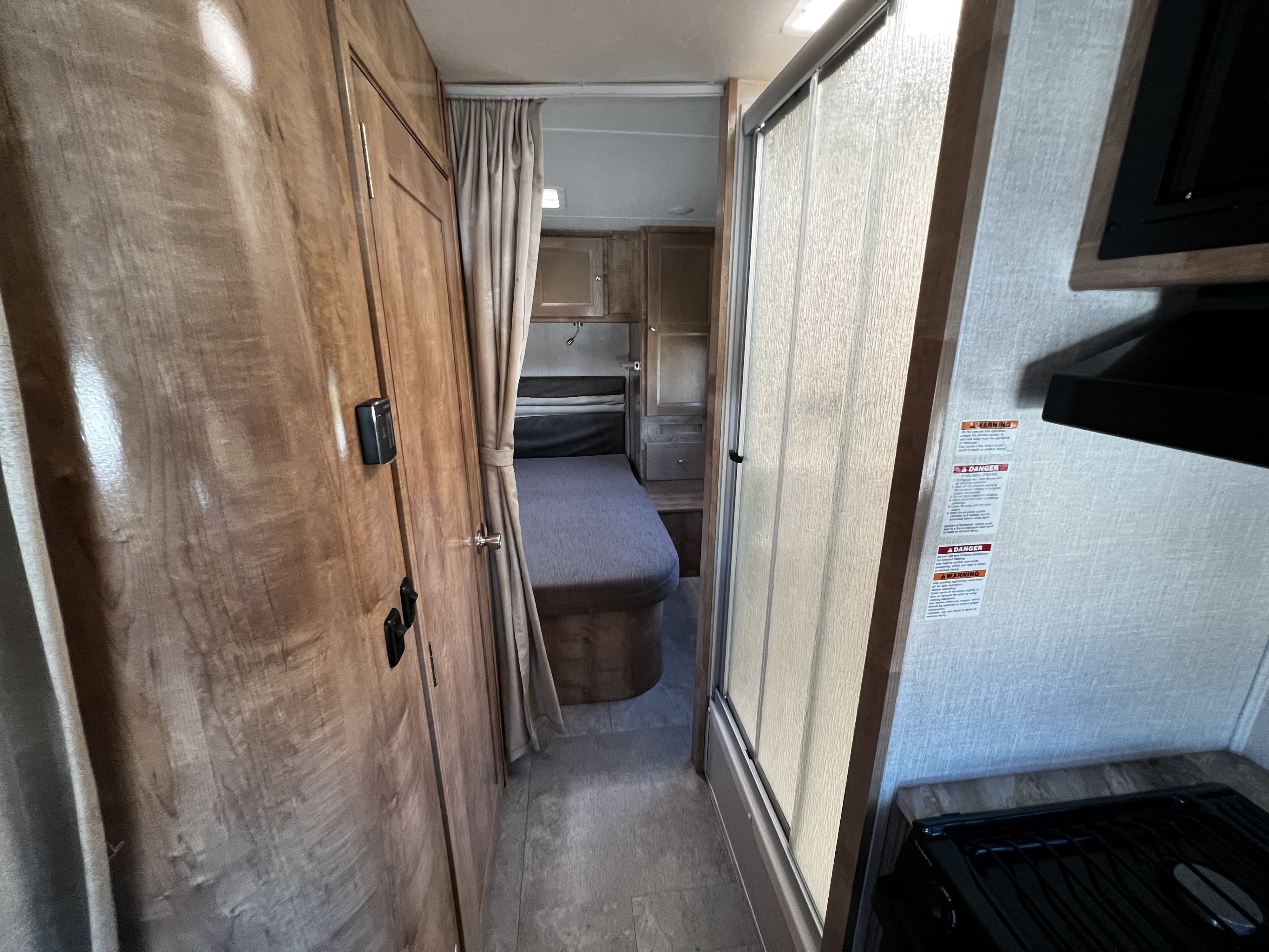 Explore a modern RV rental: compact kitchen, shower with textured glass door, leading to a cozy bedroom with bed.. Forest River Coachmen Leprechaun 2020