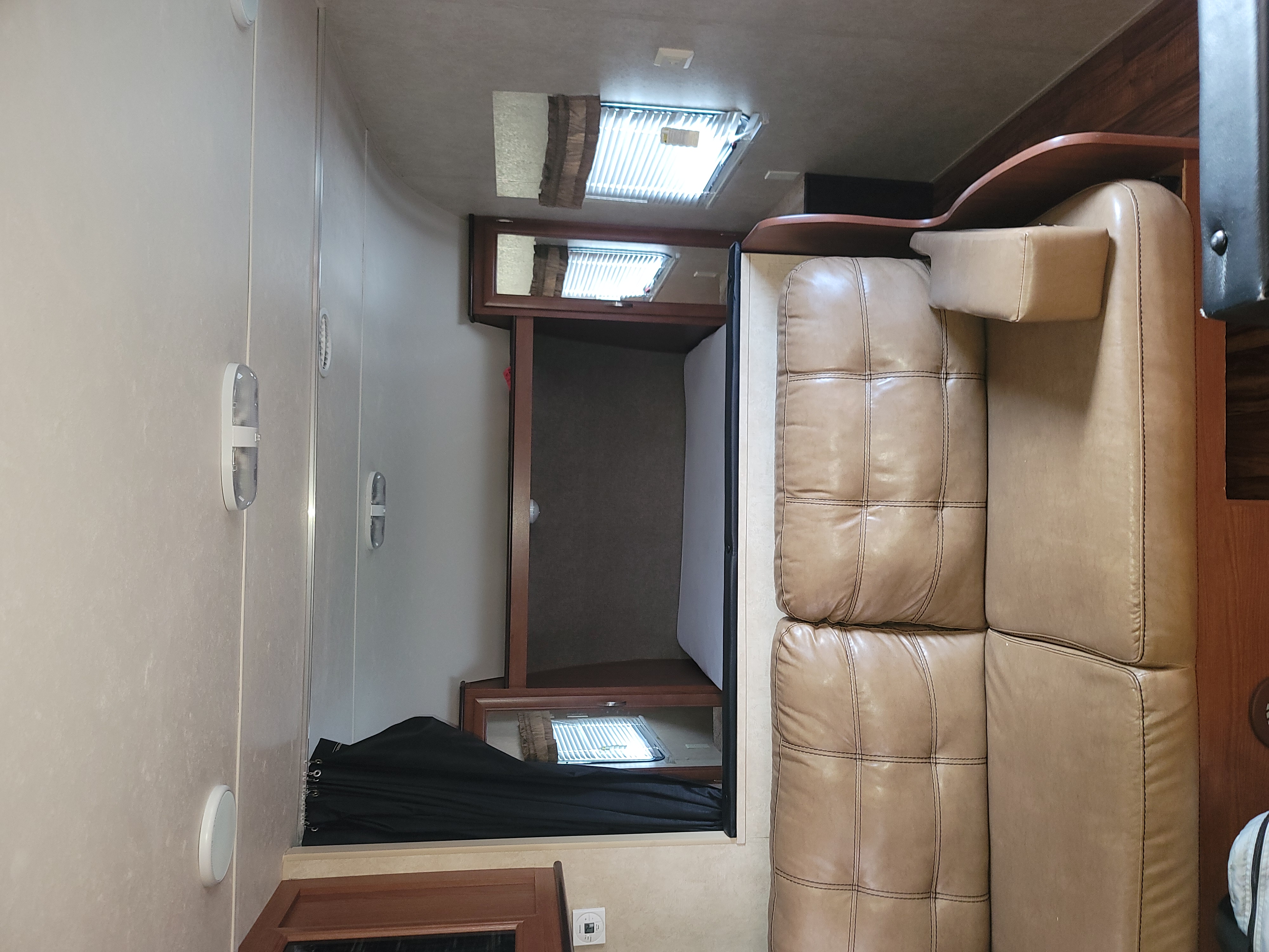 Bright RV rental interior featuring a large, tufted light brown leather sofa, windows, and wood cabinetry.. Forest River Salem 2016