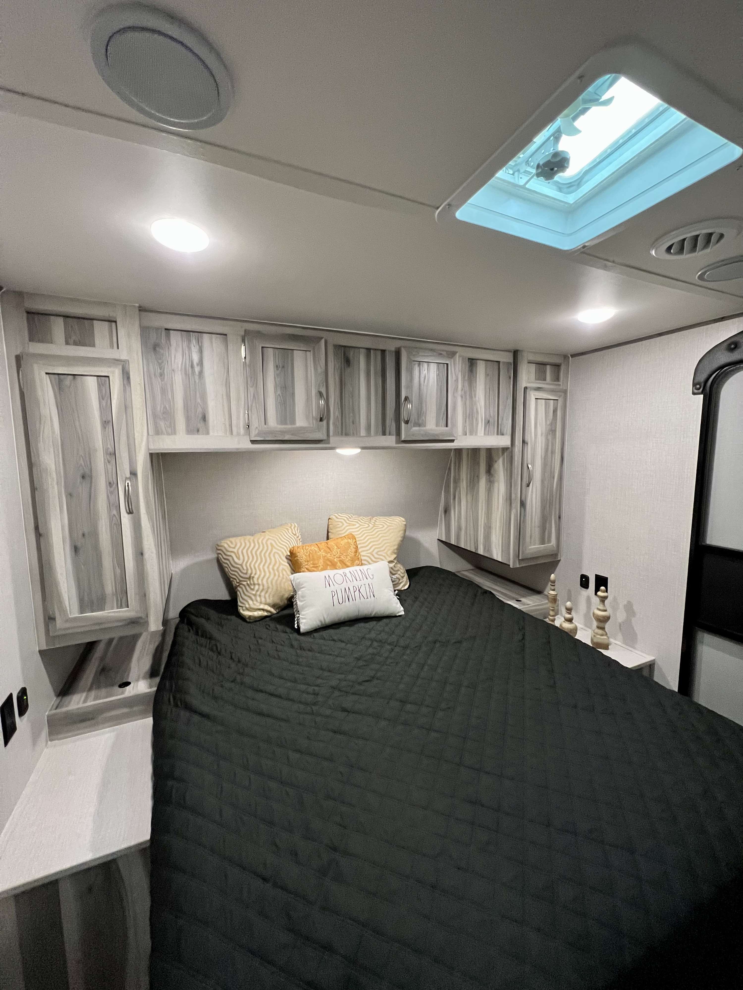 Cozy RV rental bedroom with a black quilted bed, overhead cabinets, built-in nightstands, and a ceiling skylight and vent.. Dream 290DBS 2022
