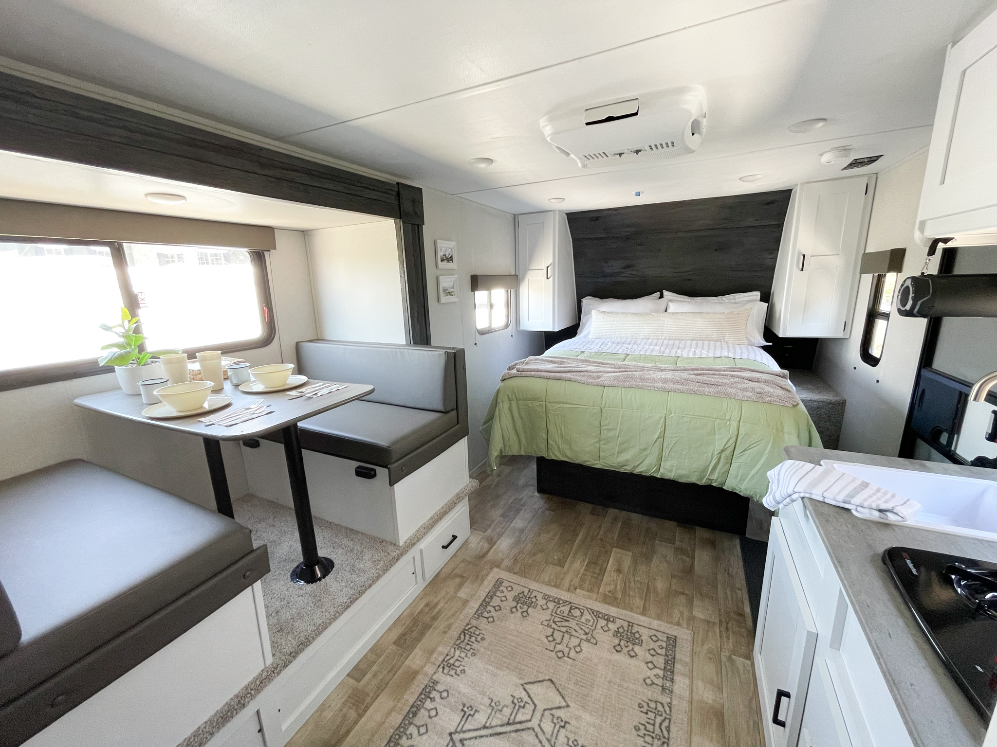 Modern RV rental interior with a comfy bed, dining booth, and compact kitchen. Light and airy living space.. Keystone RV Hideout 2022