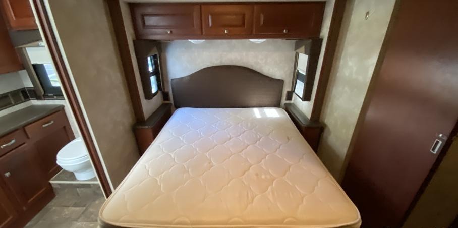 RV rental interior shows a compact bedroom with a bed, overhead cabinets, and an adjacent bathroom with a visible toilet.. Itasca Sunstar 2013
