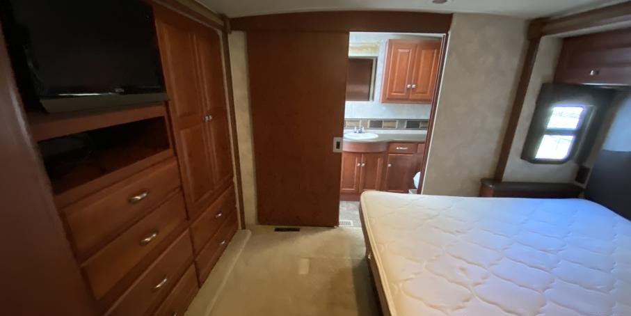 RV rental bedroom with bed, TV, wood cabinets, and a sliding door leading to the attached bathroom.. Itasca Sunstar 2013