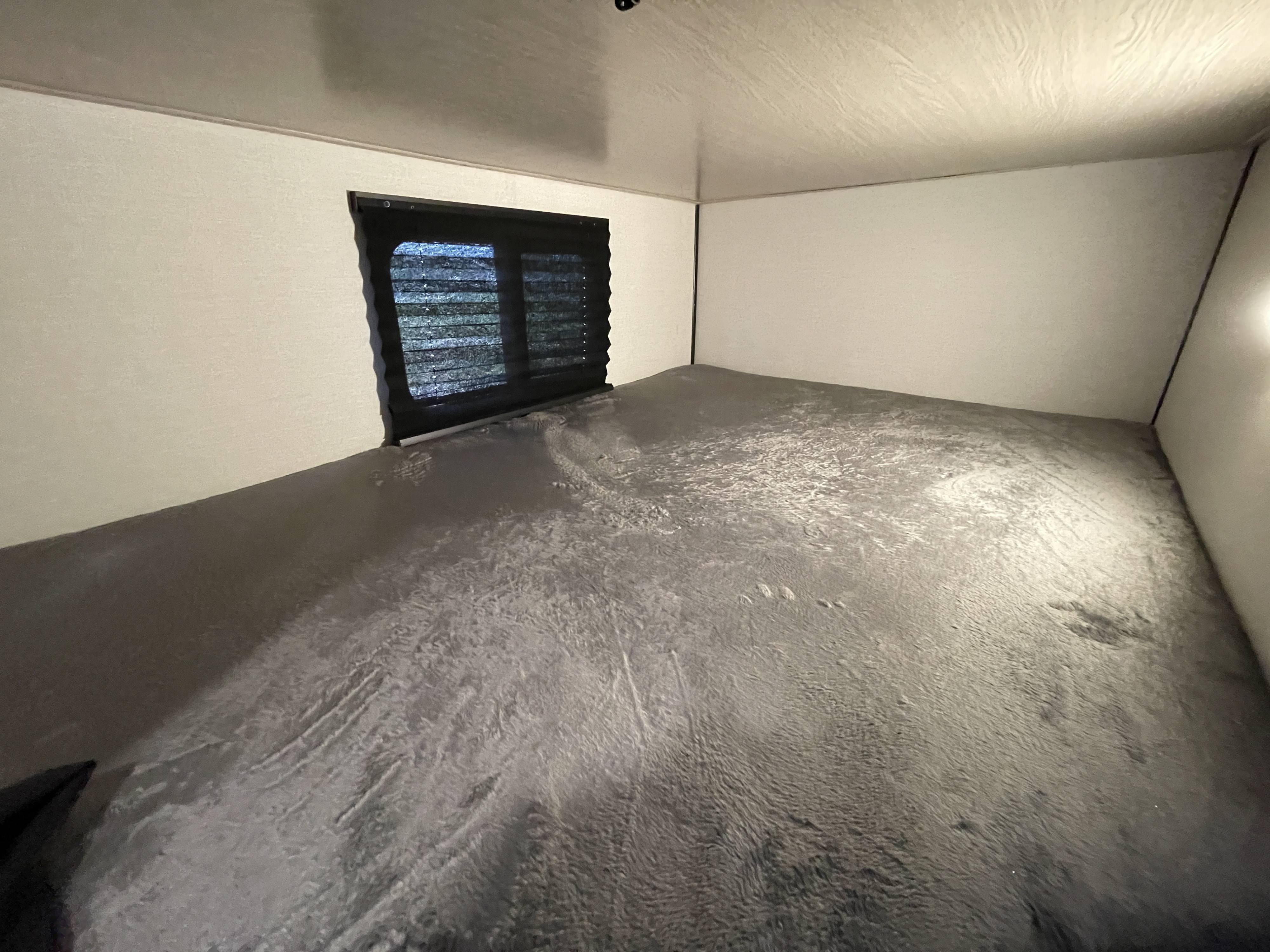 Inside an RV rental: a spacious, low-lying grey bunk bed with a window and dark blinds.. Coachmen Apex 2022