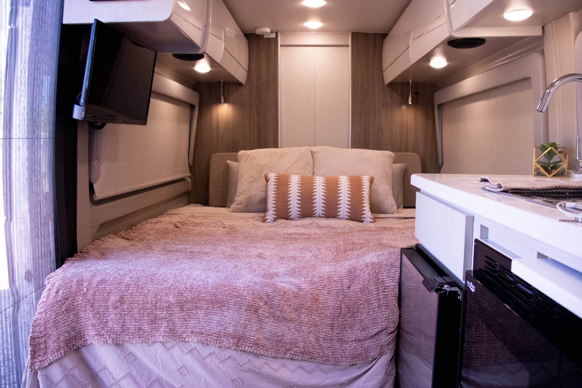 Explore this cozy RV rental interior: comfortable bed, compact kitchen, and TV. Perfect for road trip adventures.. Thor Other 2023