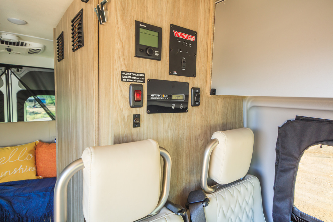 RV rental camper van interior with an advanced control panel for solar and utilities. Cozy seats and a bed visible.. Winnebago Solis 2022