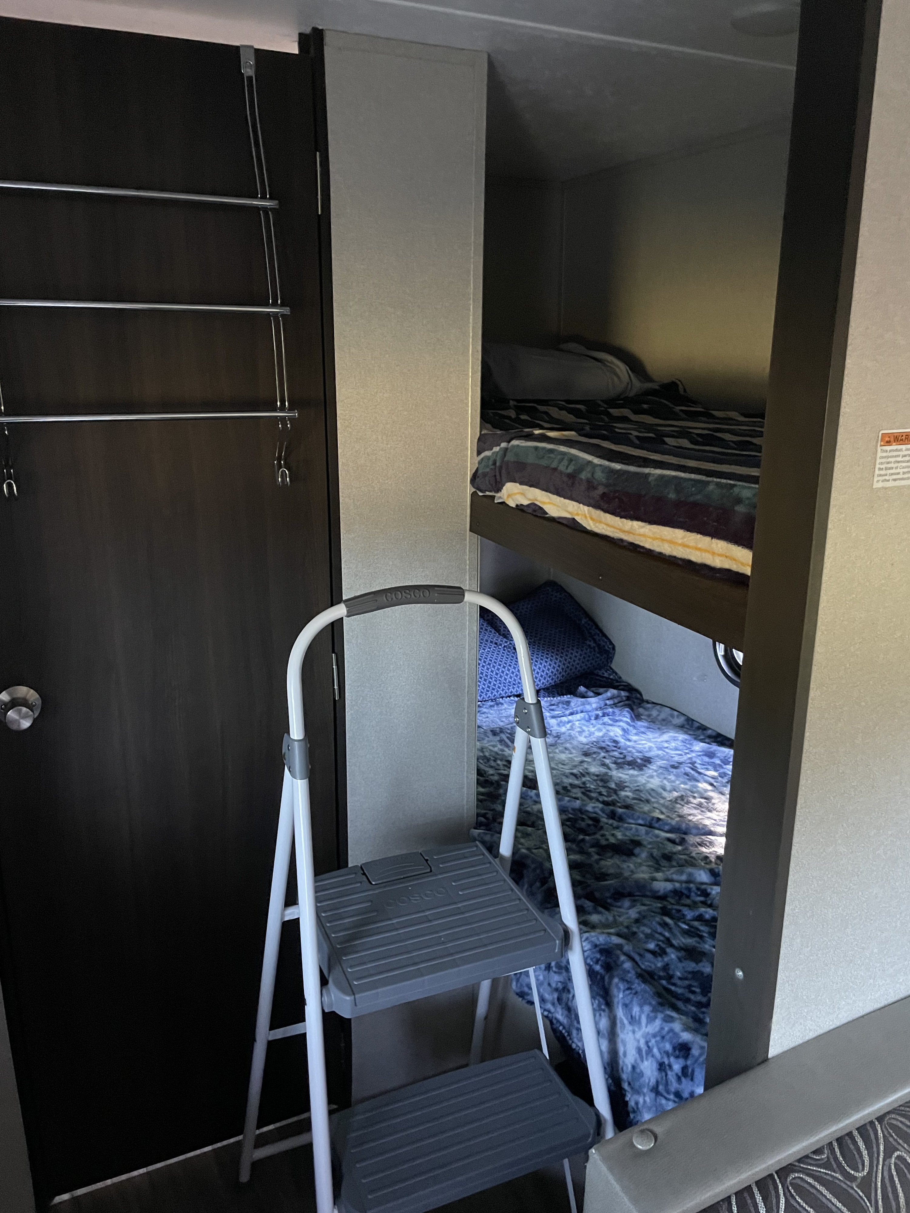 View inside an RV rental, showing stacked bunk beds, a step stool, and an over-the-door rack on a dark closet door.. Keystone RV Springdale Mini 2019