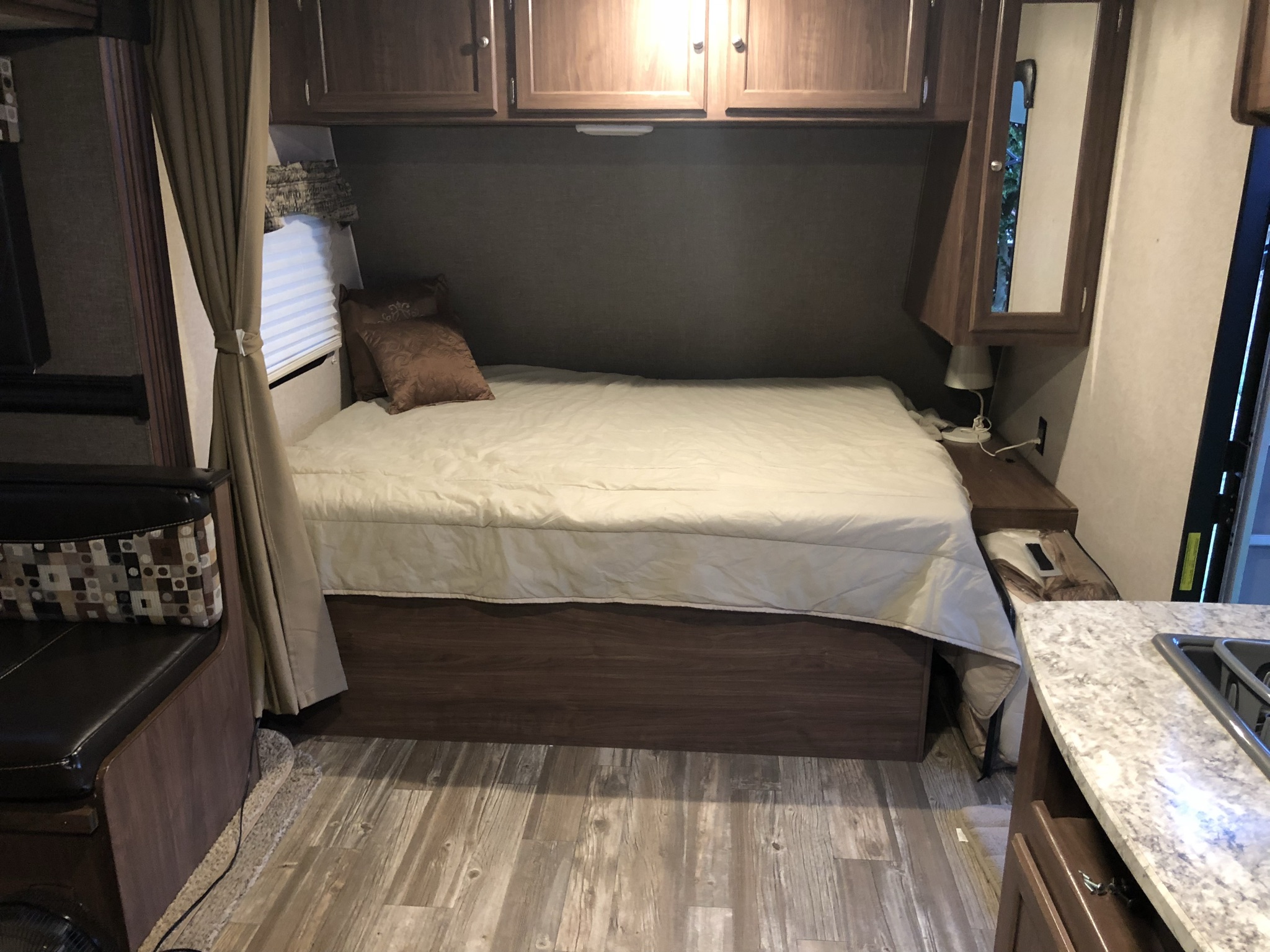 Compact RV rental interior featuring a cozy bedroom area with a bed, cabinets, and seating, plus a glimpse of the kitchen.. Heartland RVs Pioneer Toy Hauler 2017
