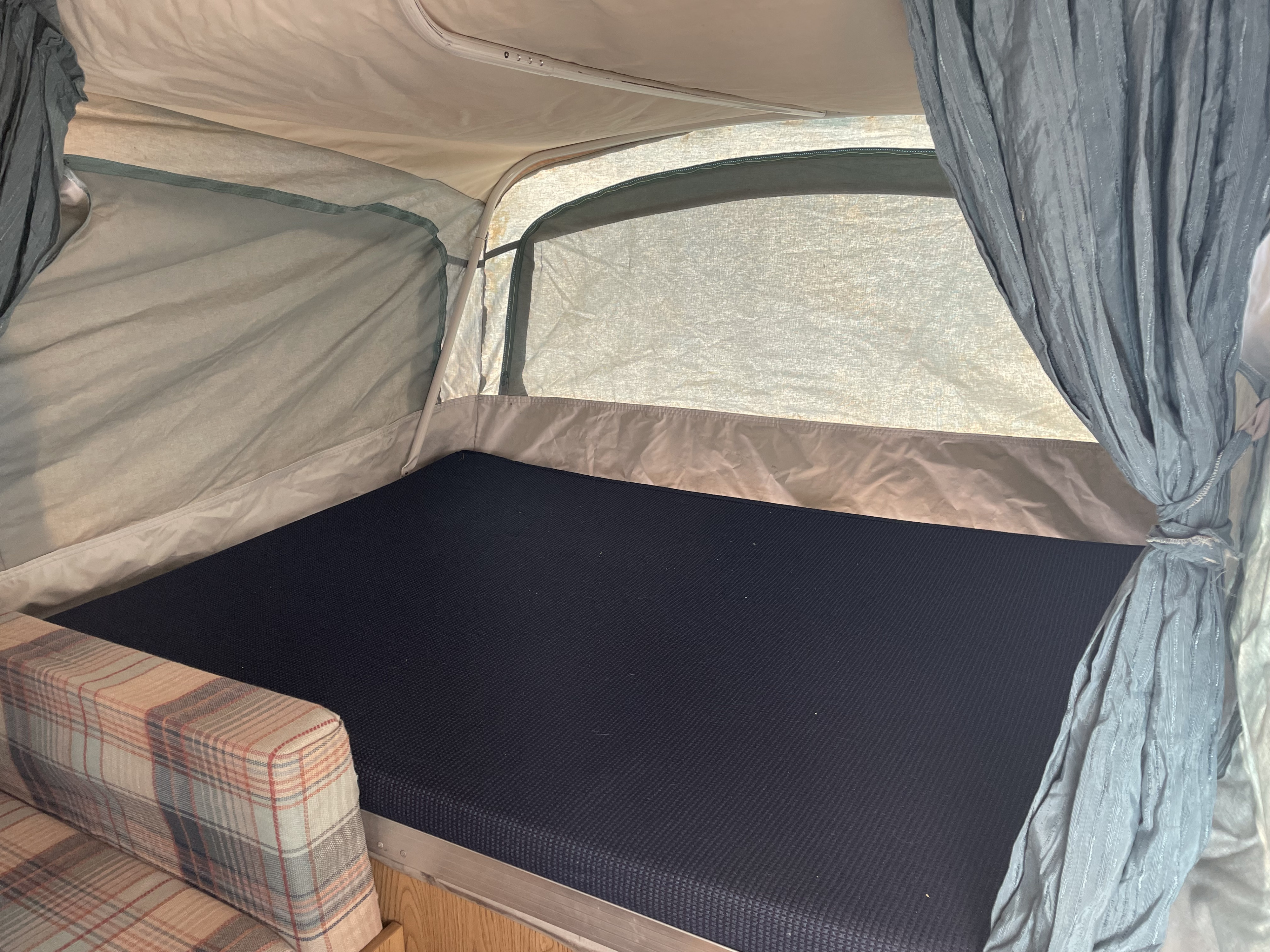 Cozy pop-up camper interior with a dark bed and plaid couch, ideal for an RV rental.. Coleman Destiny Roanoke 1992