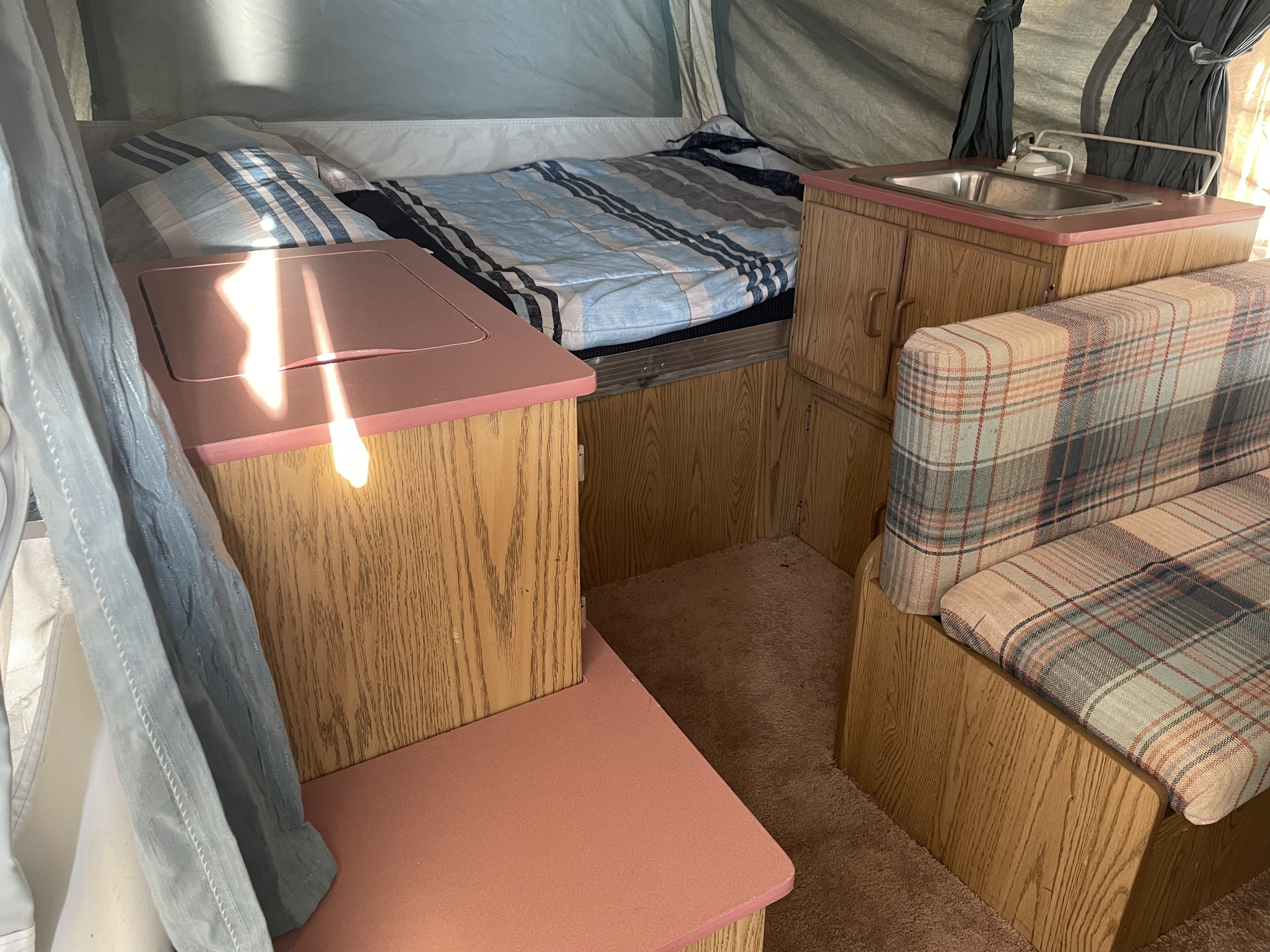 Pop-up camper RV rental interior with striped bed, sink, and plaid dinette seating.. Coleman Destiny Roanoke 1992
