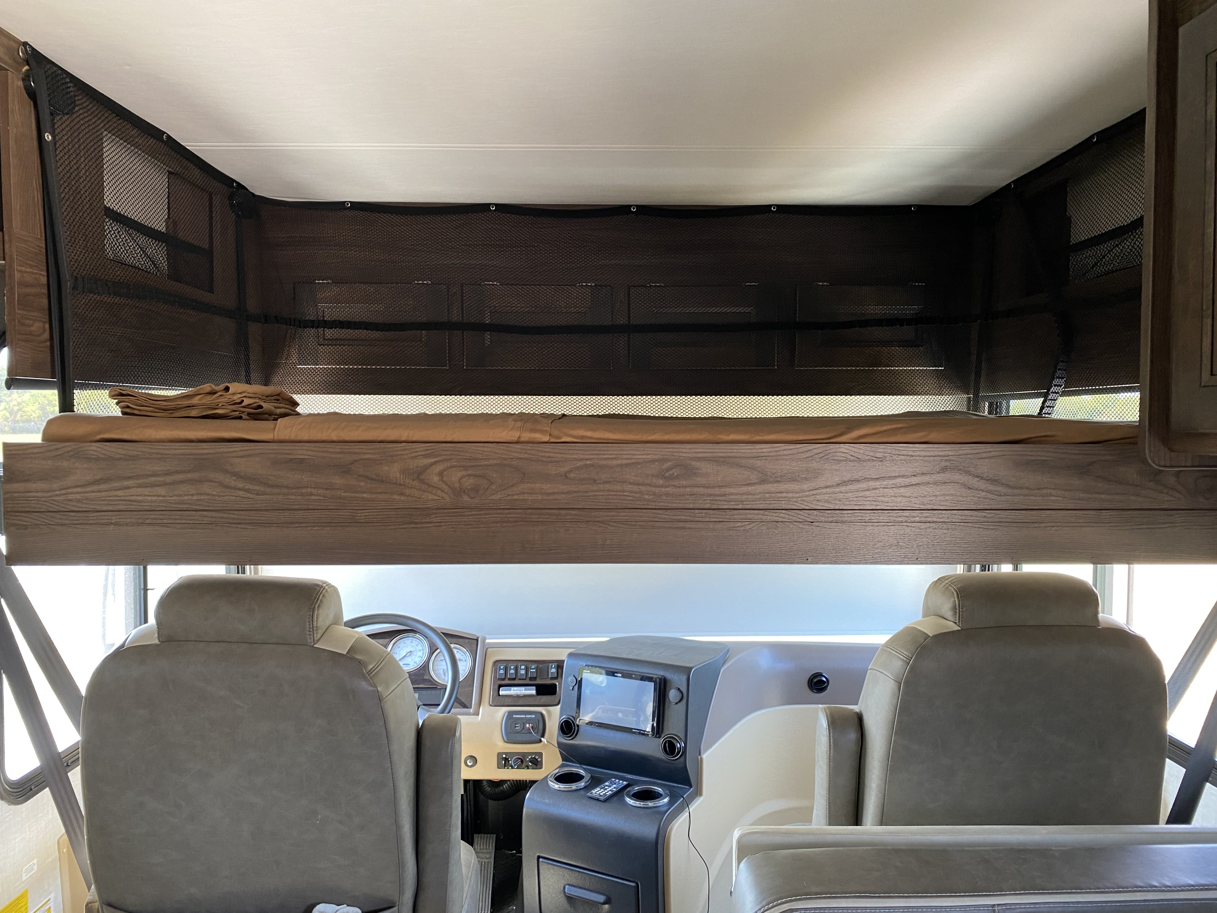 RV rental interior: Overhead bunk with safety net above the cockpit, featuring driver/passenger seats and dashboard.. Coachmen Sports Coach 339DS 2019