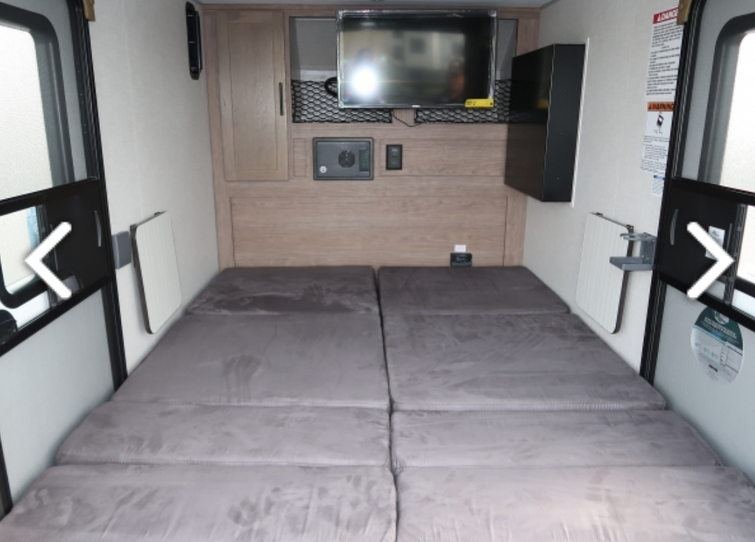 Compact RV rental interior showing two large floor mattresses, a mounted TV, storage cabinet, and foldable side tables.. Forest River NOBO 10.6 2022
