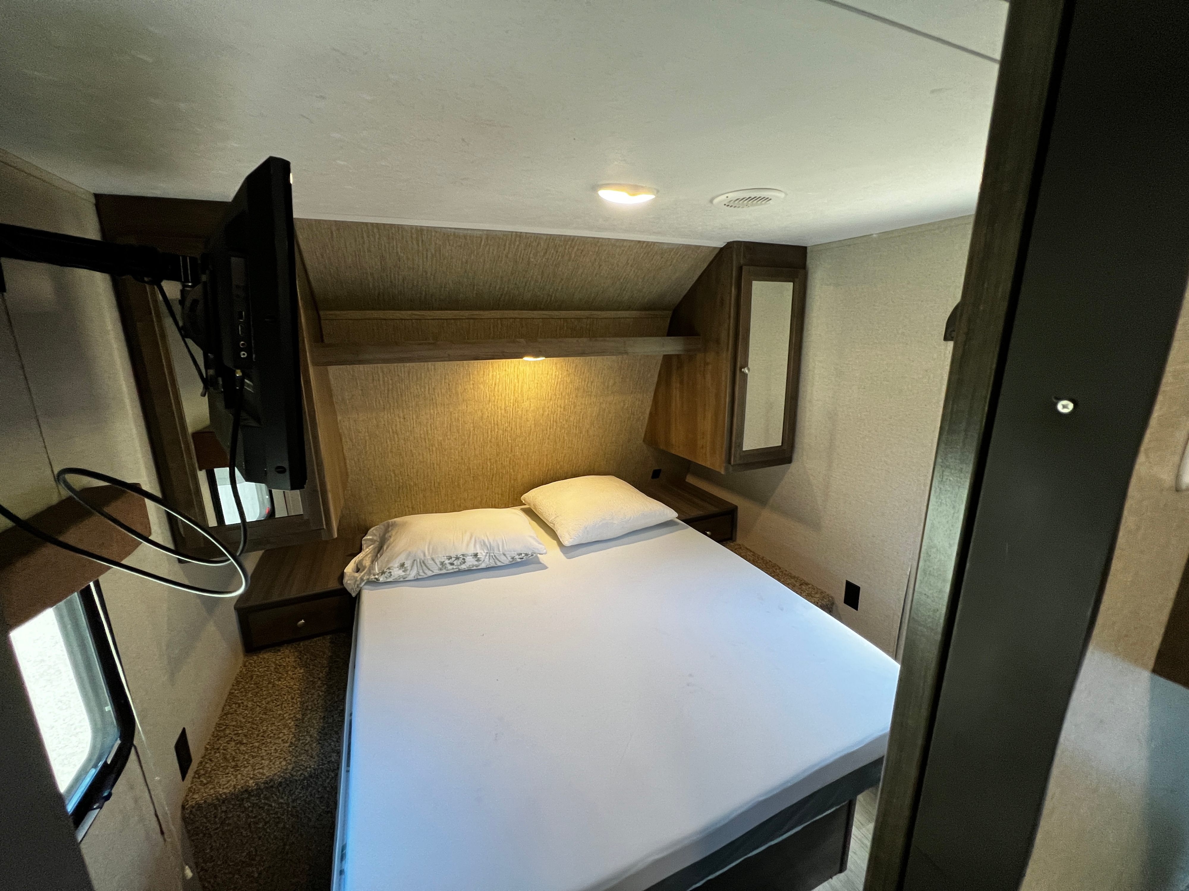 Cozy RV rental bedroom featuring a mounted TV, comfortable bed, overhead lighting, and built-in storage.. Coleman 285BH 2018