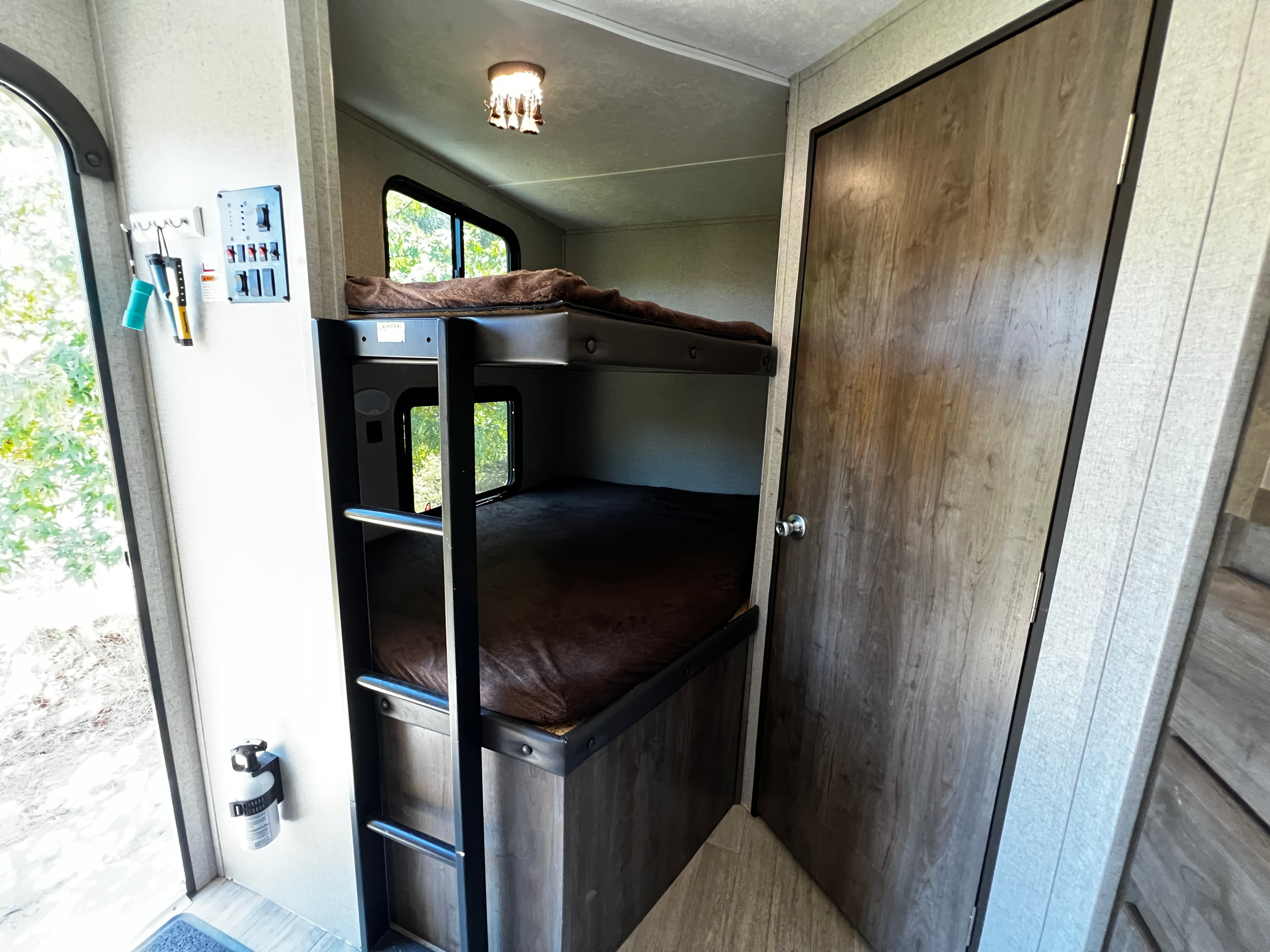 RV rental interior: cozy bunk beds with brown bedding, an adjacent door, control panel, and window view, ideal for travel.. Coleman 285BH 2018