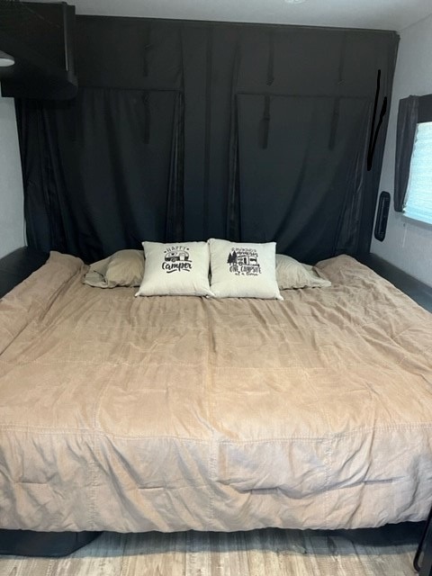 Cozy RV rental bedroom showing a large bed with a beige comforter and two decorative camping pillows.. Forest River Cherokee 2021