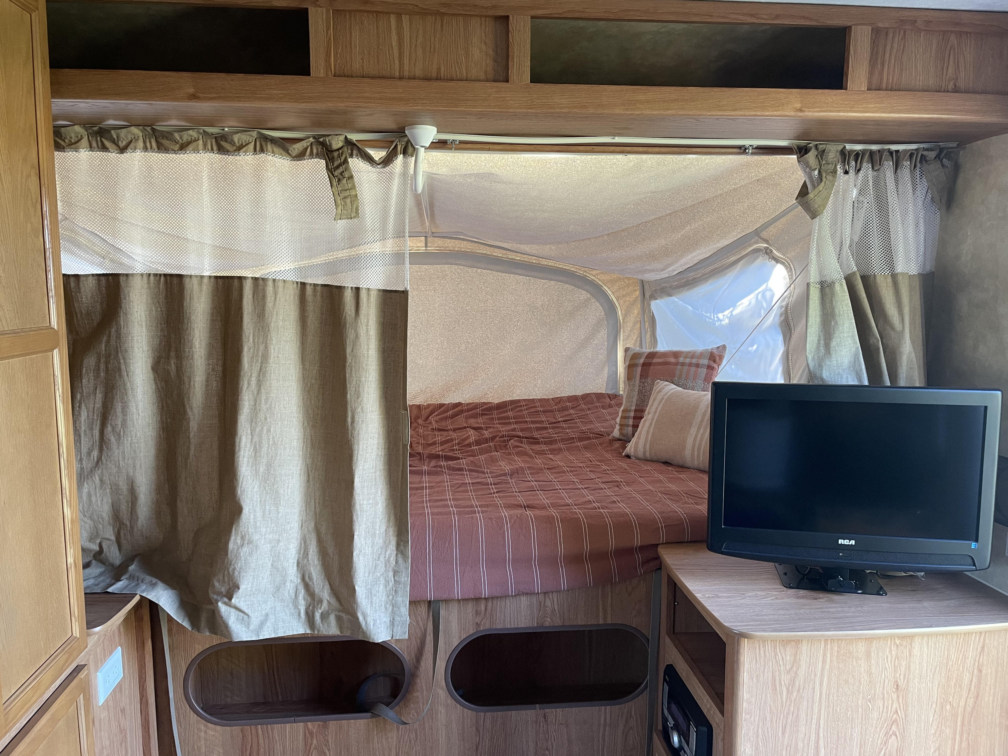 RV rental interior: A cozy pop-up camper bedroom with a striped bed, privacy curtains, and a TV setup.. Jayco Jay Feather Exp 2010