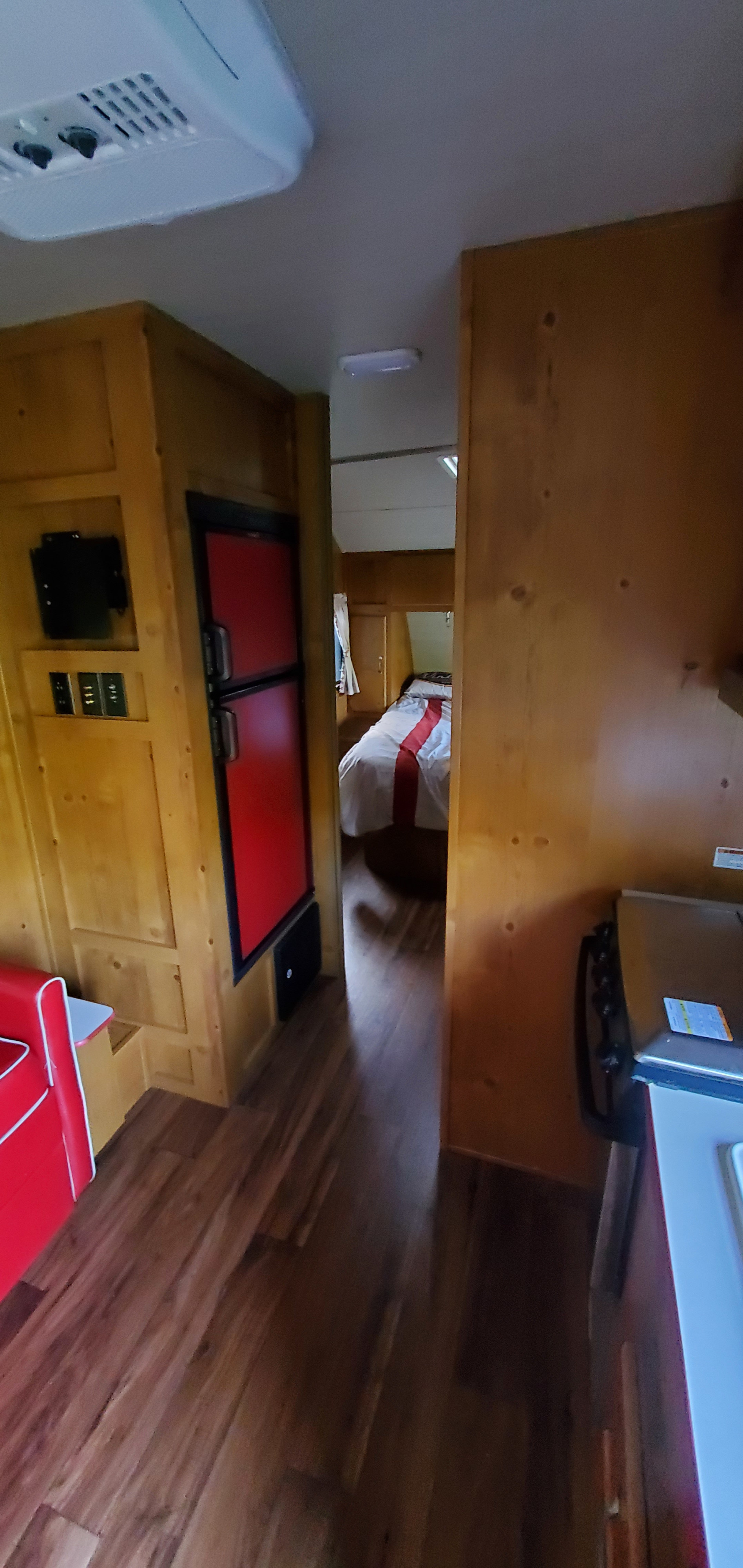 Inside an RV rental: a wooden interior featuring a red refrigerator, a cozy bed in the back, and a compact kitchen.. Gulf Stream Vintage Friendship 2019
