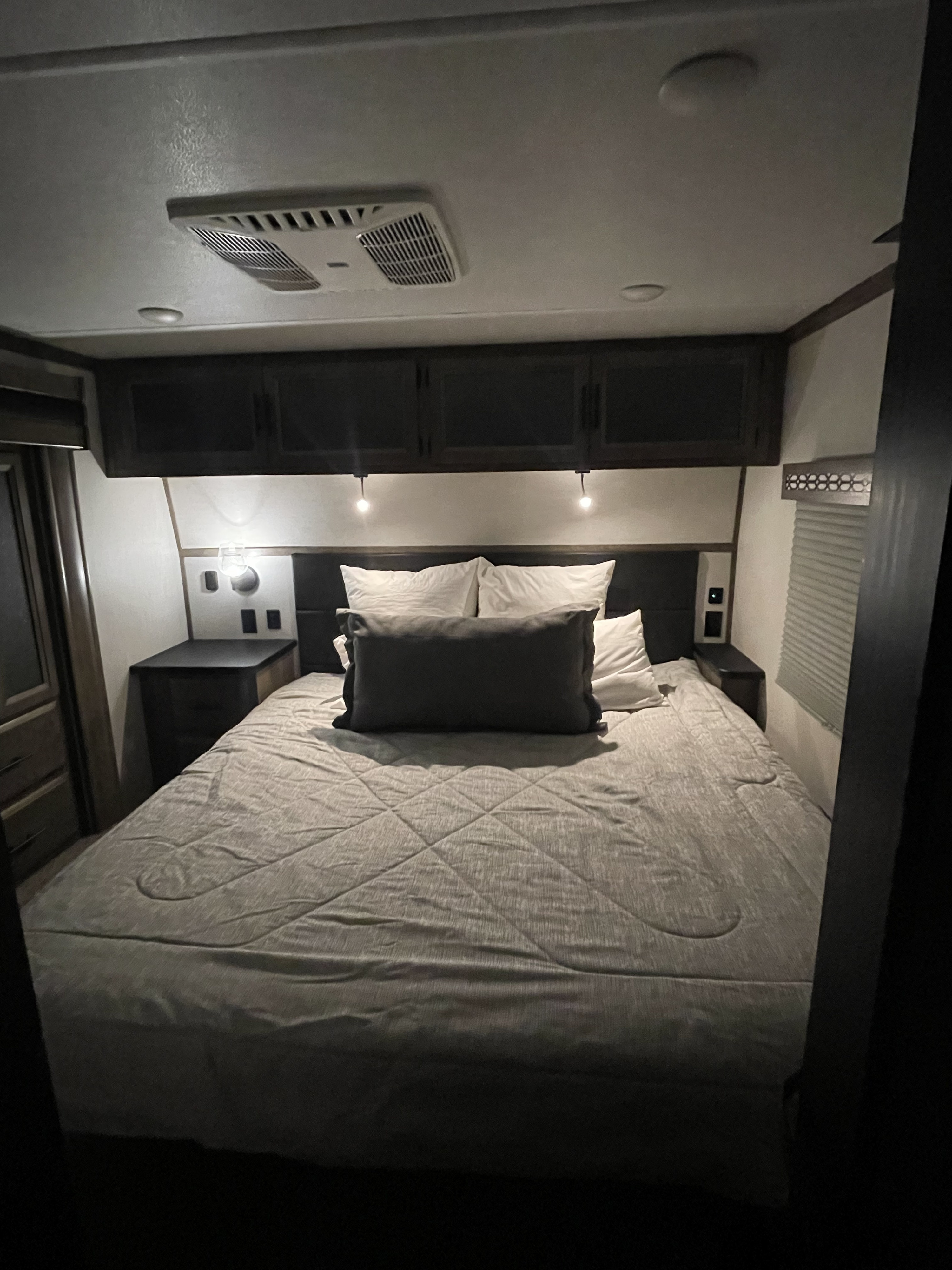Cozy RV rental bedroom with a large bed, overhead storage, and soft bedside lighting, perfect for comfortable rest on your journey.. Forest River Vengeance 2021