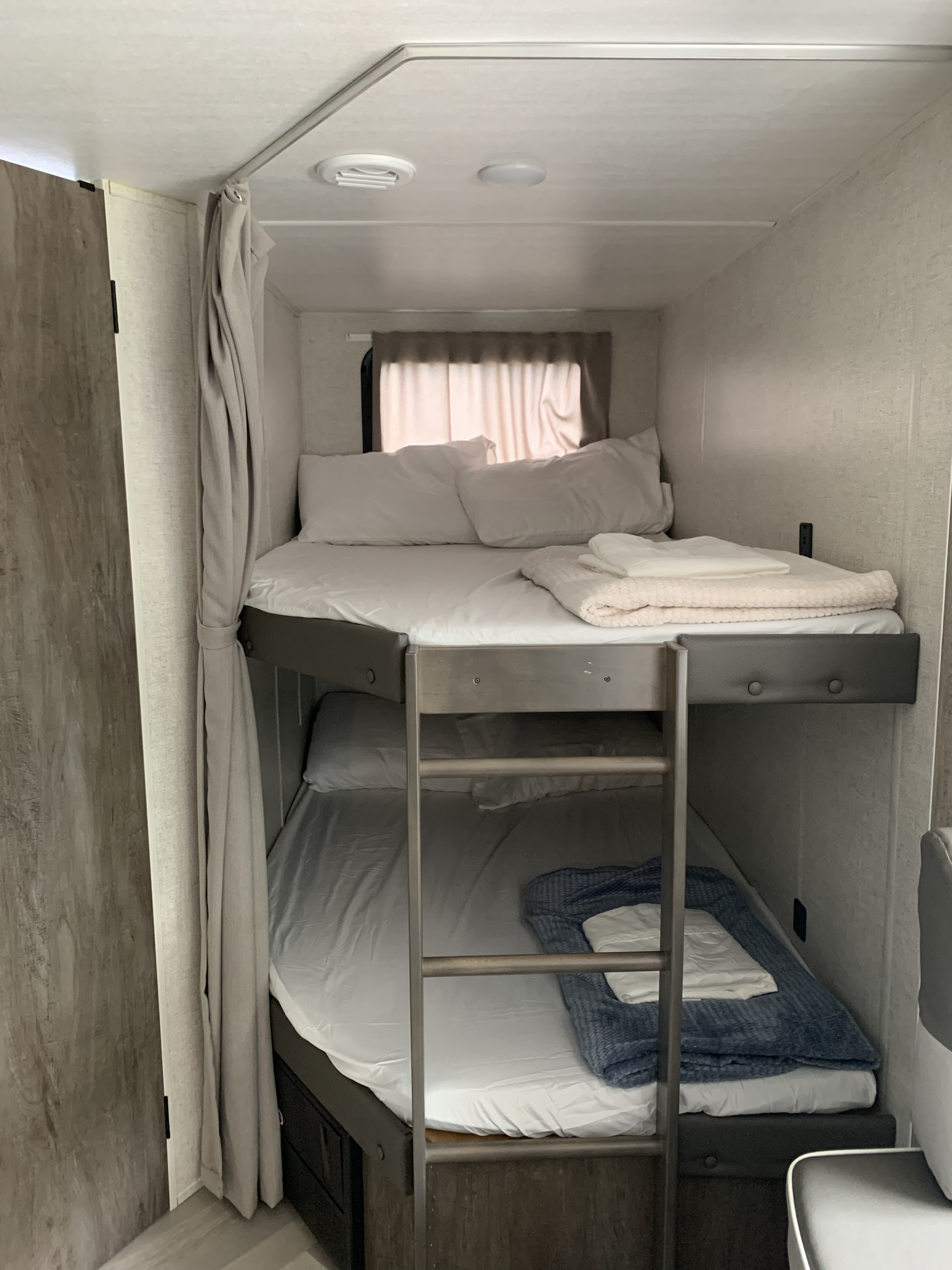 Interior of an RV rental showing cozy bunk beds with ladder, privacy curtains, and fresh linens for travelers.. Forest River Wildwood X-Lite 2021