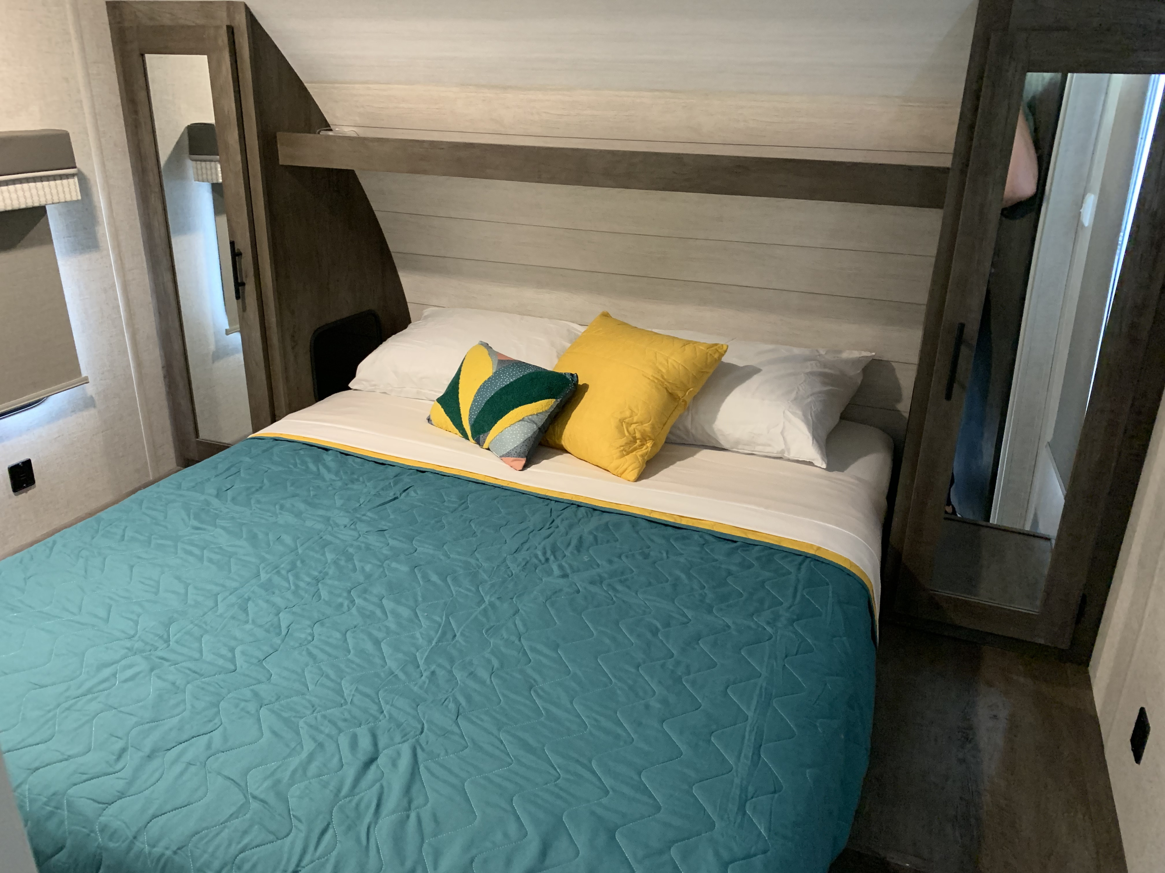 Comfortable RV rental bedroom with quilted teal comforter, vibrant pillows, and built-in storage.. Forest River Wildwood X-Lite 2021