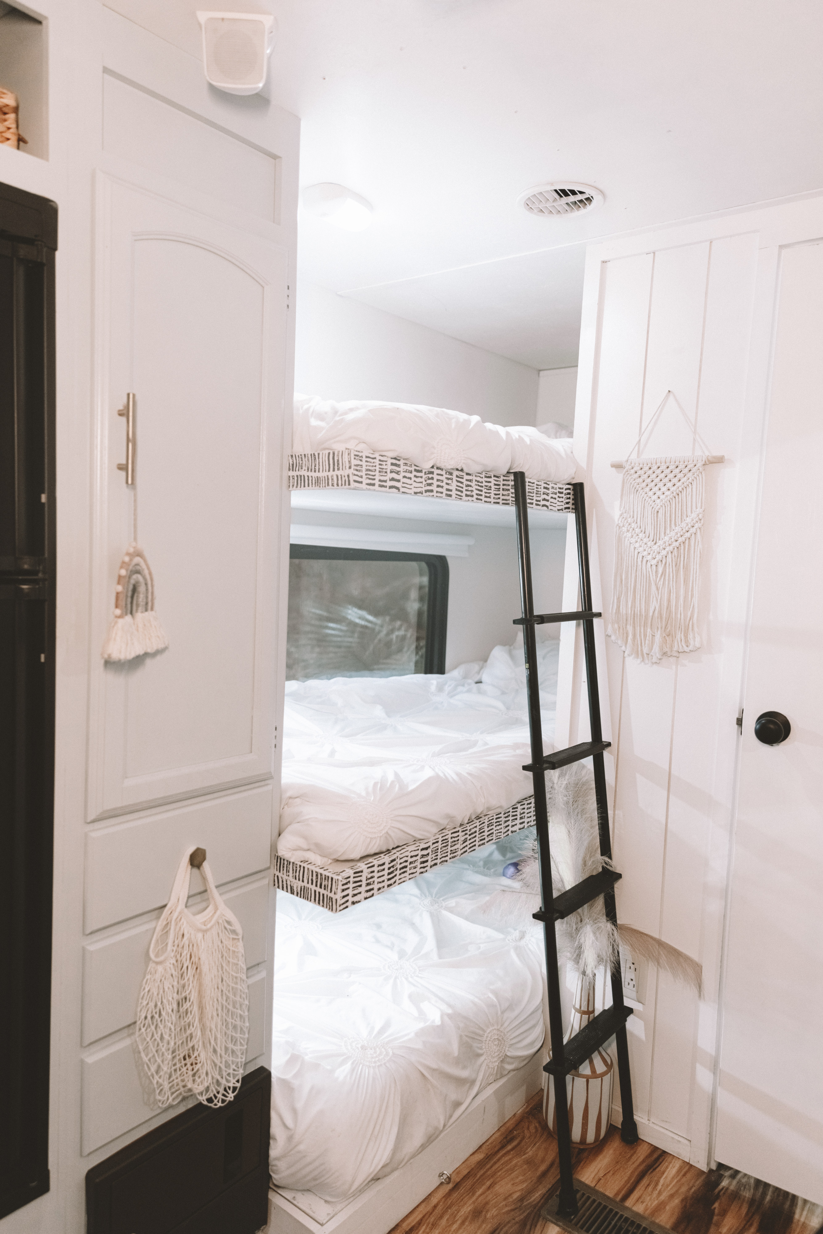 Inside a bright RV rental: three cozy bunks with white bedding, a black ladder, and wood floors. Ideal for family adventures.. Forest River Other 2013