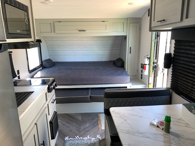 Inside a modern RV rental: compact kitchen with microwave, large bed, and dinette seating. Light wood floors and grey cabinets throughout.. Forest River Salem FSX 2022