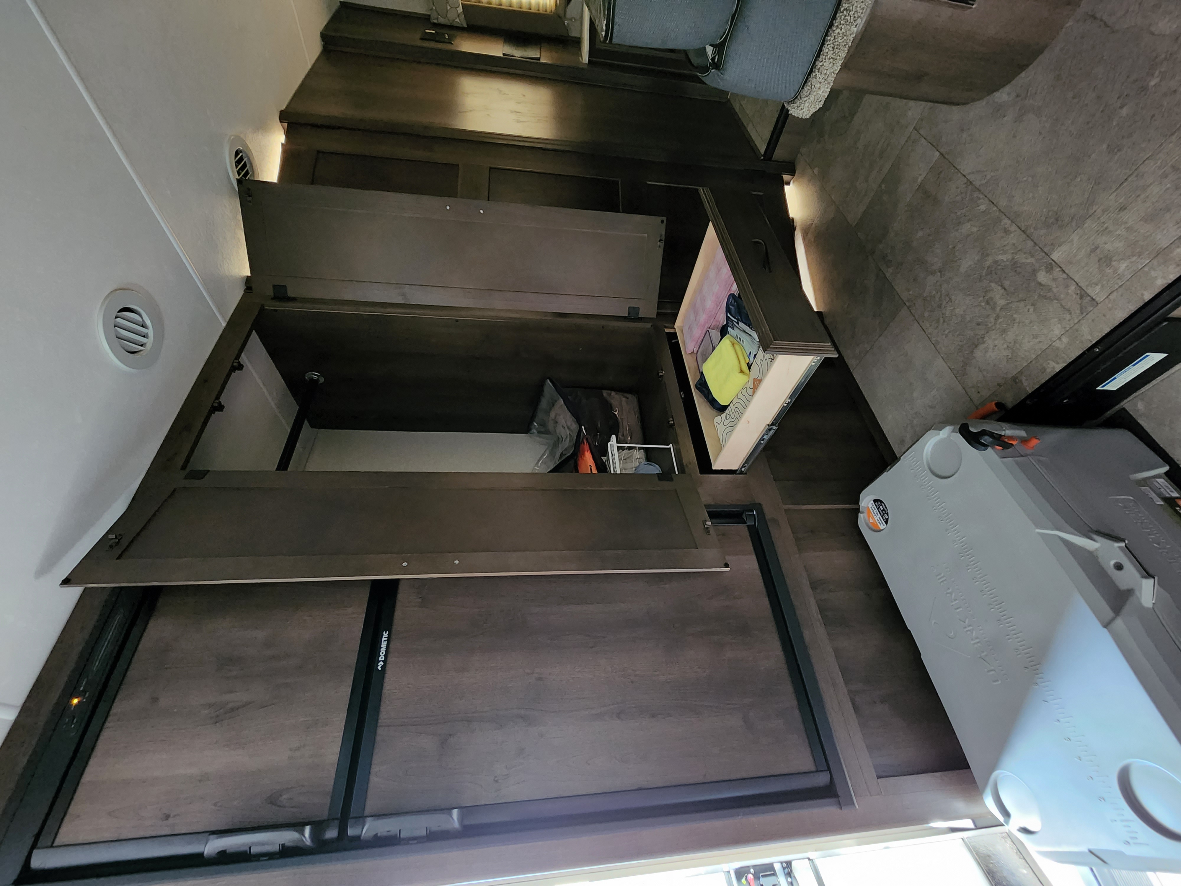 Open storage in an RV rental reveals a Dometic cooler and organizational space for belongings, typical for mobile living.. Forest River Coachmen Freelander 2019