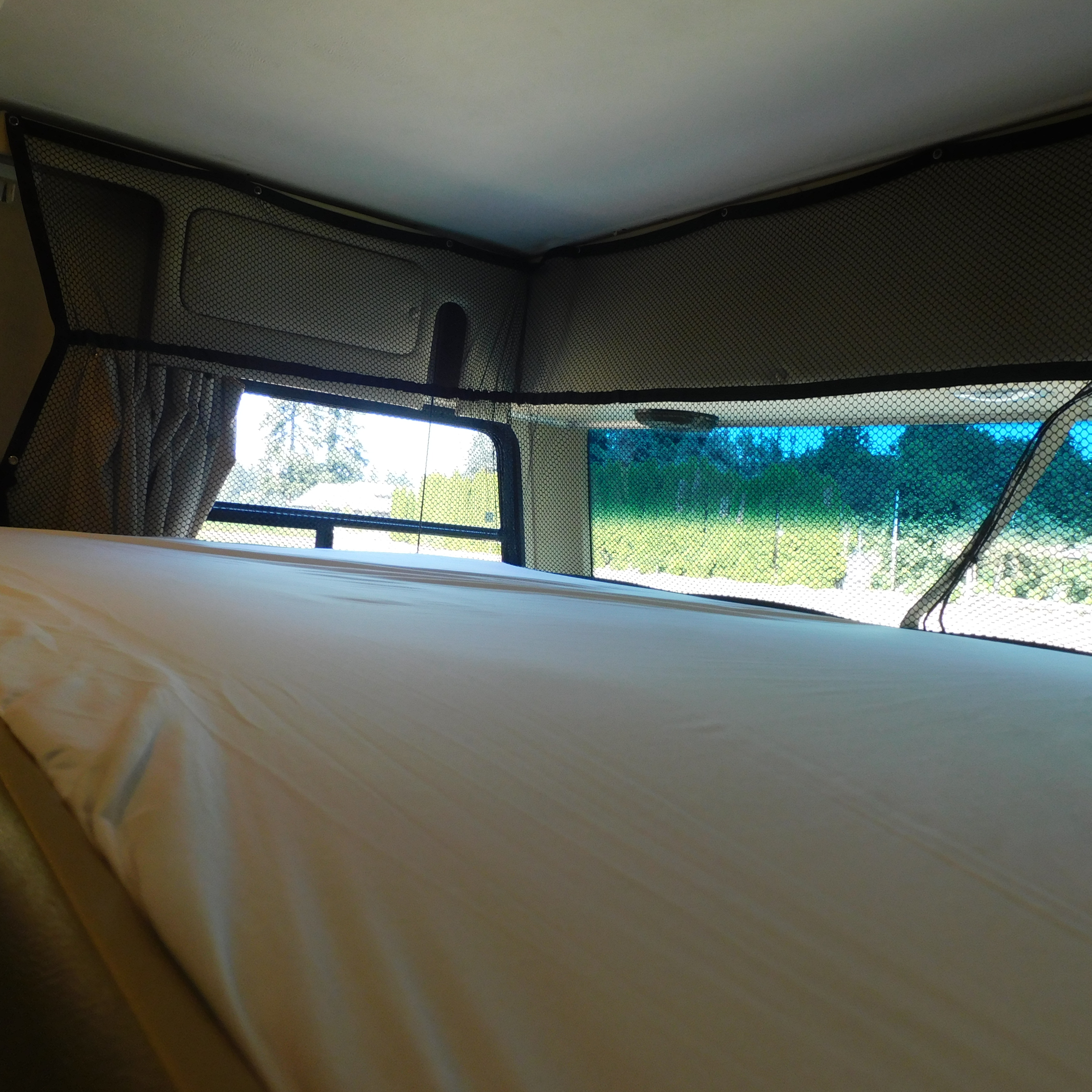 RV rental overhead bunk bed with safety net and bright outdoor view. This cozy sleeping area is ready for adventure.. Coachmen Pursuit 2017
