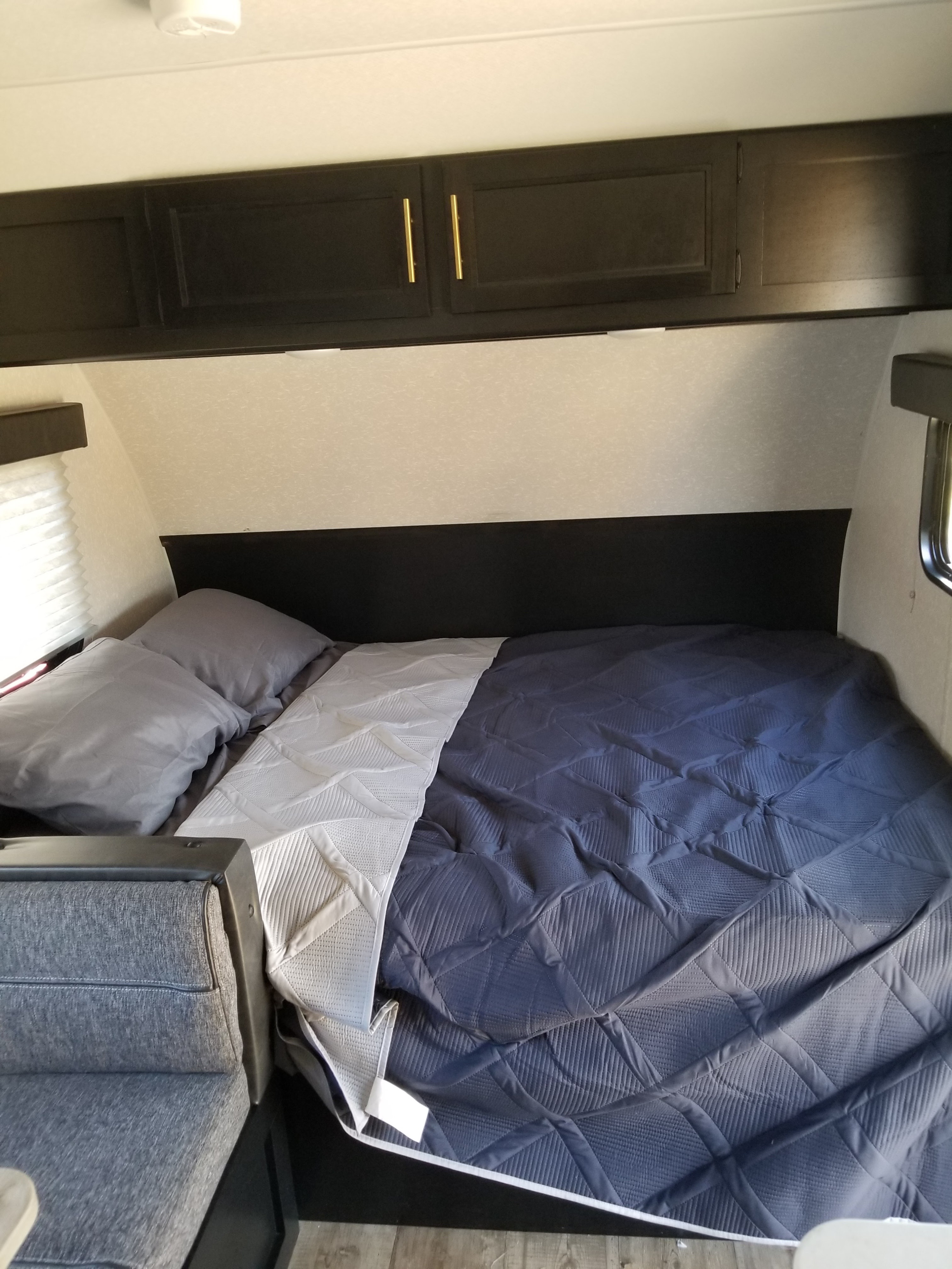 Inside an RV rental: a modern bedroom with a blue and white quilted bed, overhead cabinets, and a gray couch.. Forest River Cherokee Wolf Pup 2022