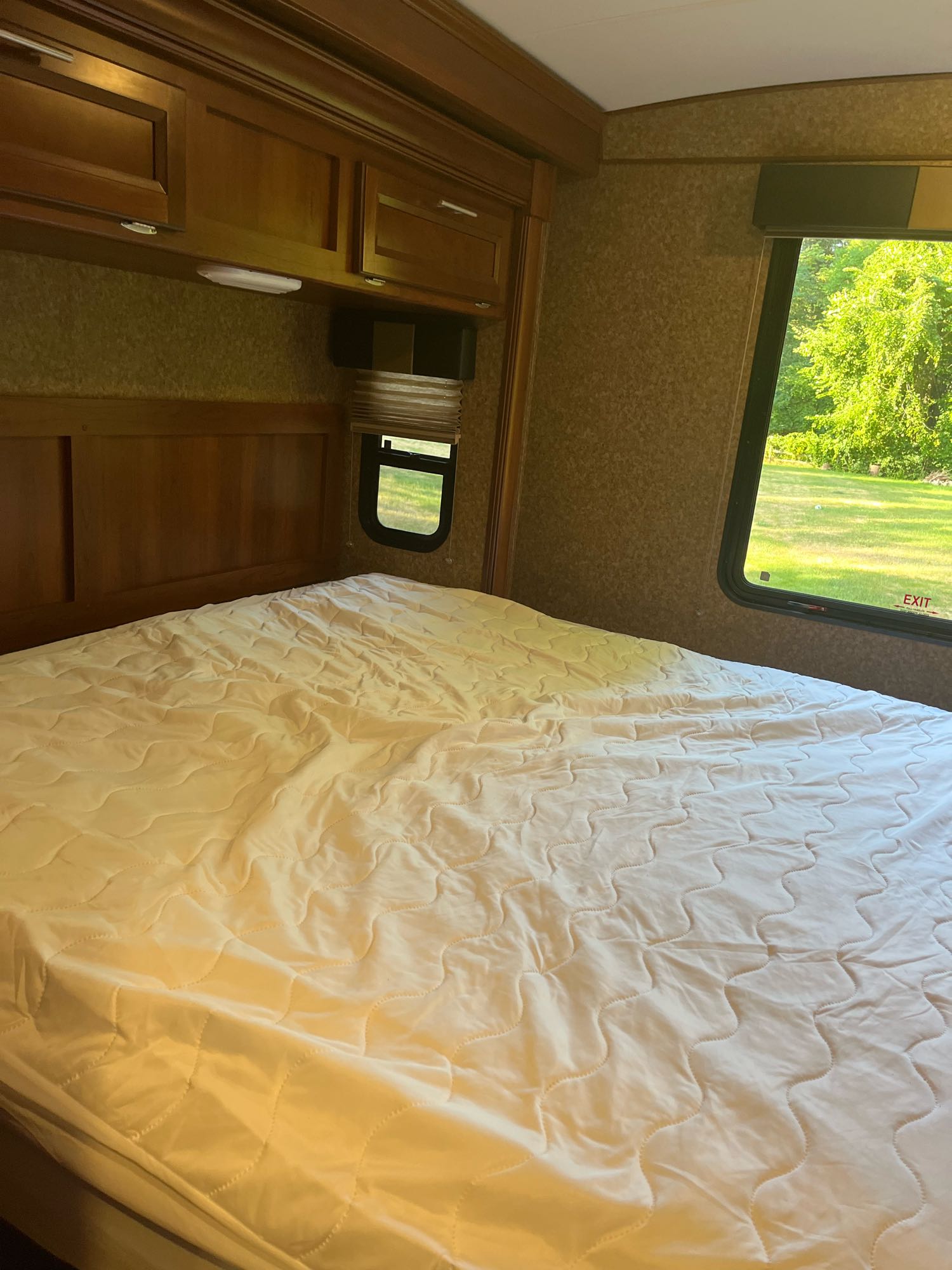 Inside this cozy RV rental bedroom: a large bed with quilted pad, wooden cabinets, and a window overlooking nature.. Forest River FR3 2015
