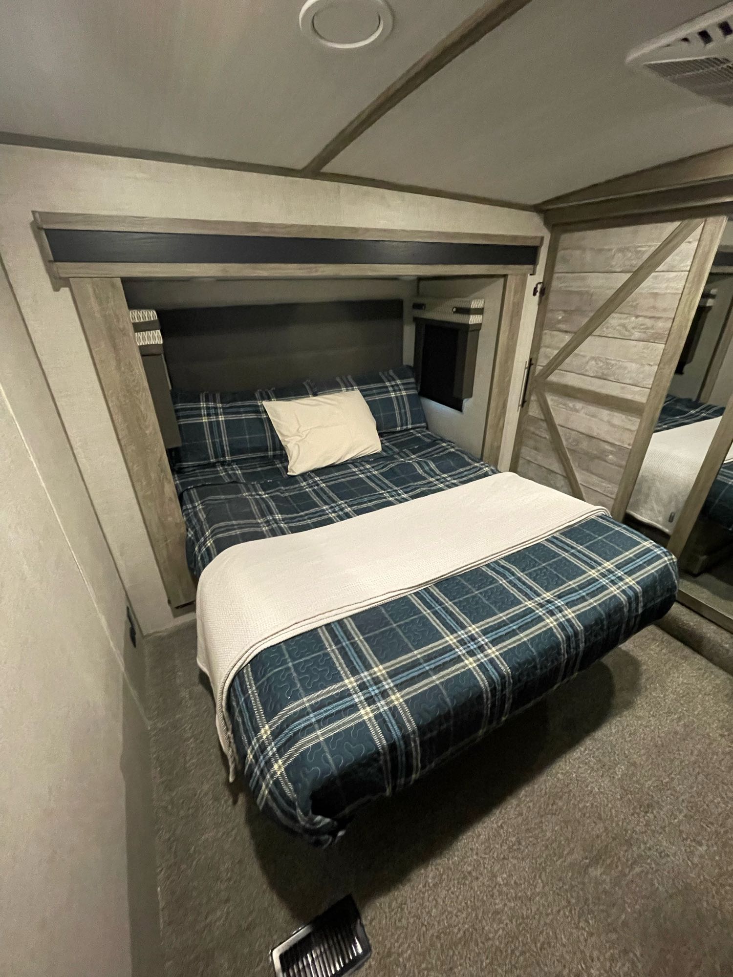 This RV rental bedroom features a comfy bed with blue plaid bedding, a white blanket, and cozy wood paneling.. Forest River Wildwood Heritage Glen 2021