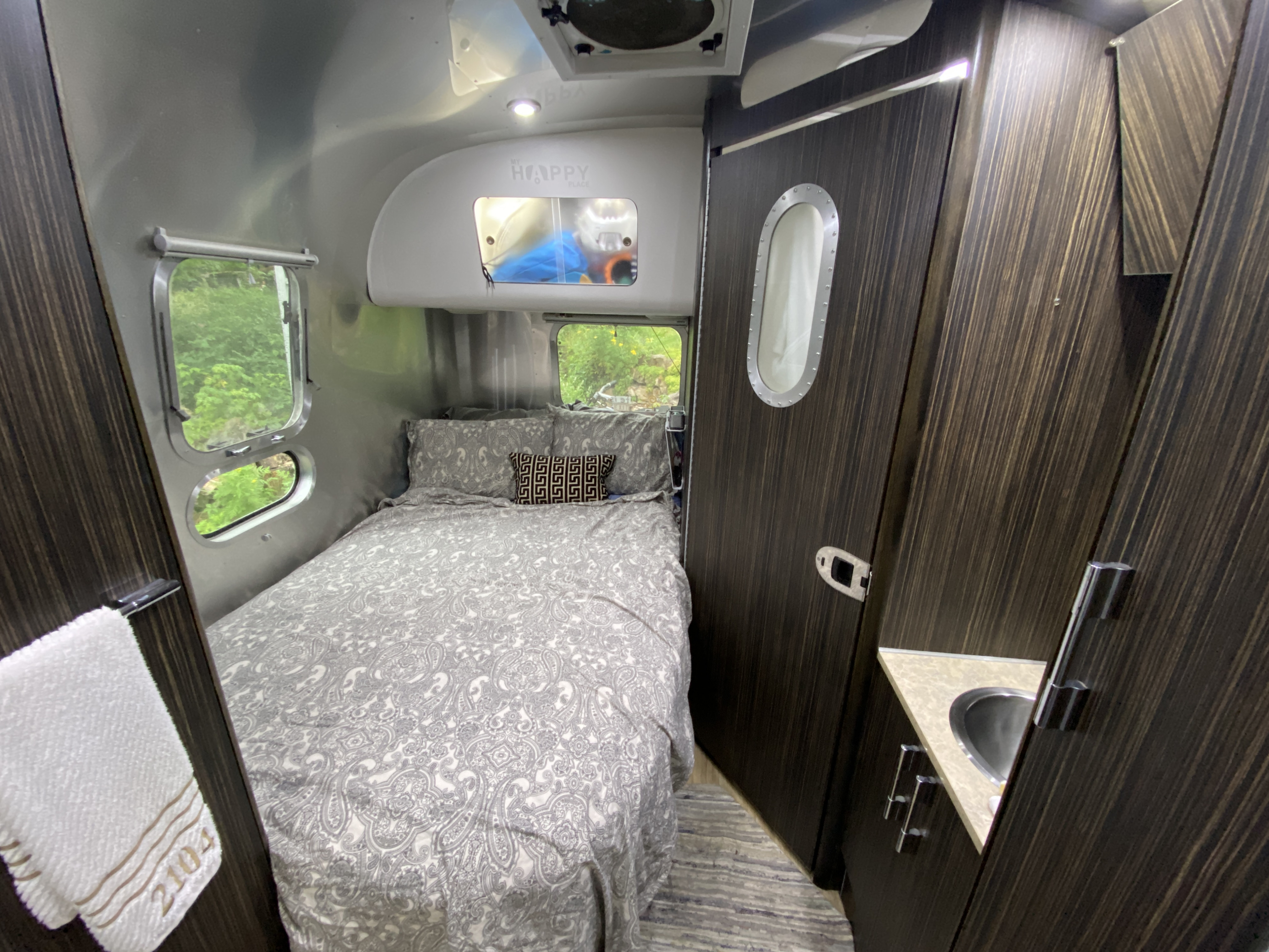 Aluminum-walled RV rental interior features a cozy bed, dark wood cabinetry, and compact sink area, perfect for small space living.. Airstream International 2014