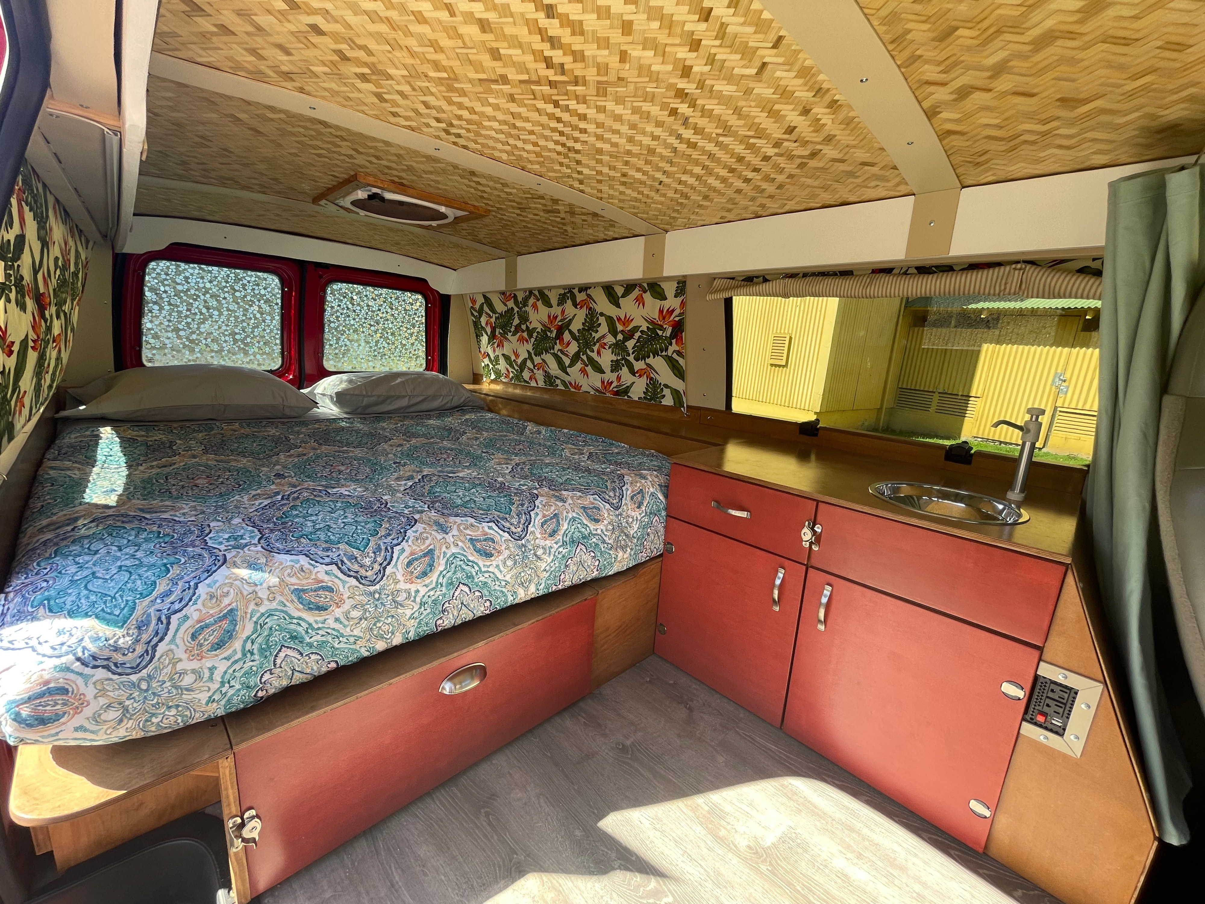 Inside this RV rental: a cozy bed with patterned bedding, woven ceiling, reddish cabinets, and a compact sink.. Ford Ford E350 2010