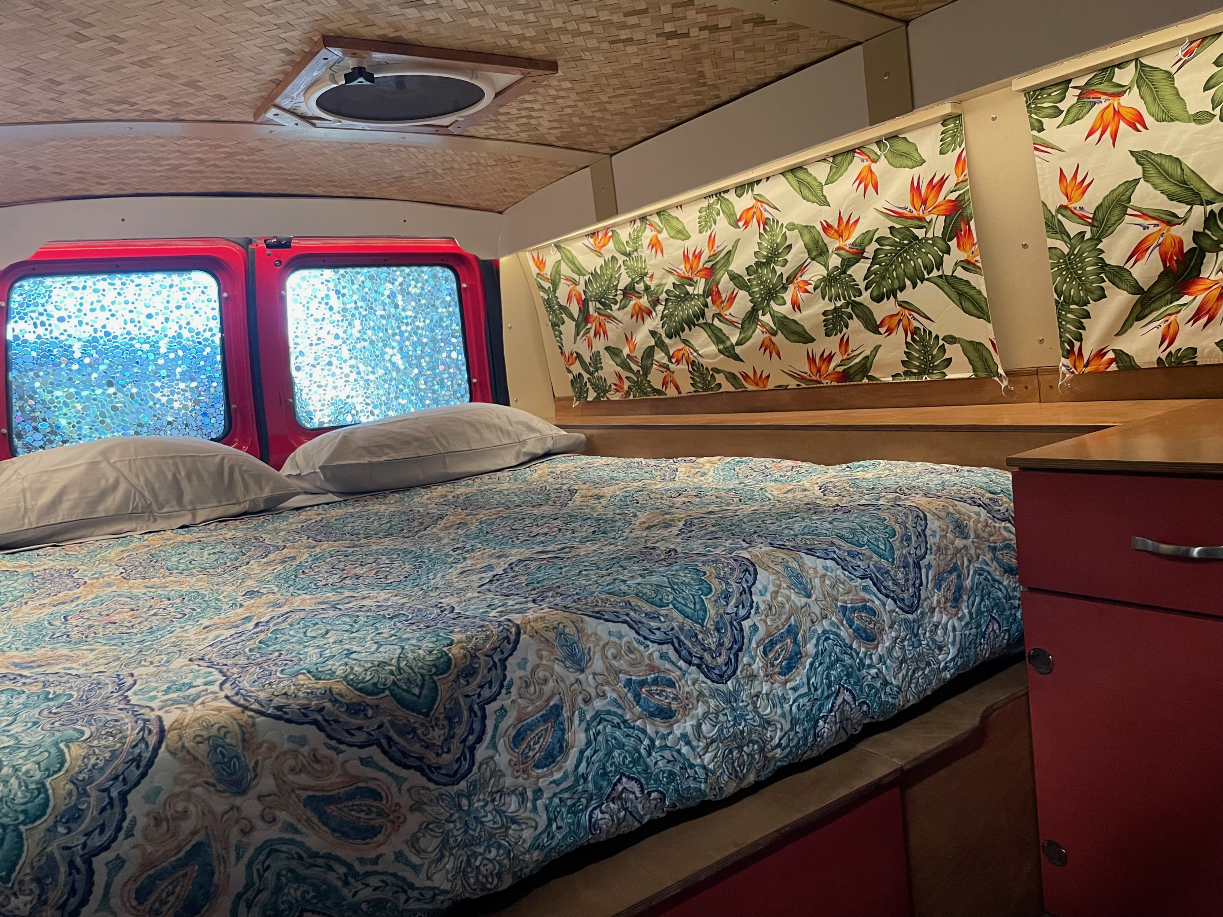 Inside a cozy RV rental: comfy bed with vibrant quilt, red window frames with textured glass, tropical curtains & bamboo ceiling.. Ford Ford E350 2010