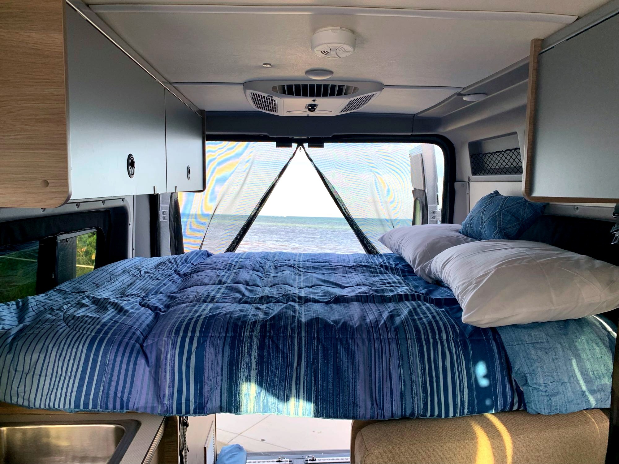 Experience an RV rental: camper van interior with a comfy bed, ocean view, storage, and AC. Ideal for seaside adventures.. Winnebago Solis 2023