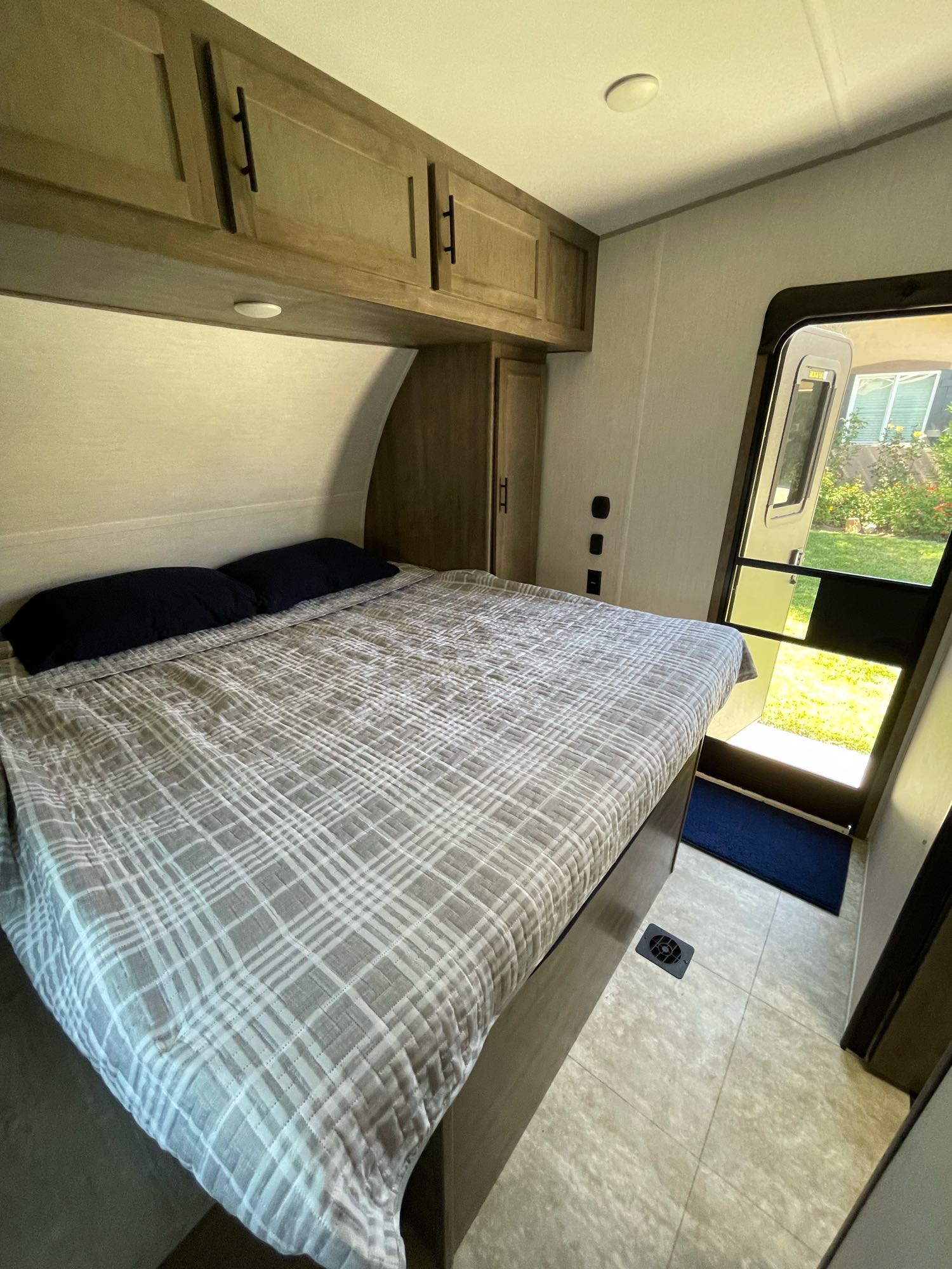 Explore this cozy RV rental bedroom. Features a large bed, cabinets, and open door offering outdoor views.. Forest River Vengeance 2022