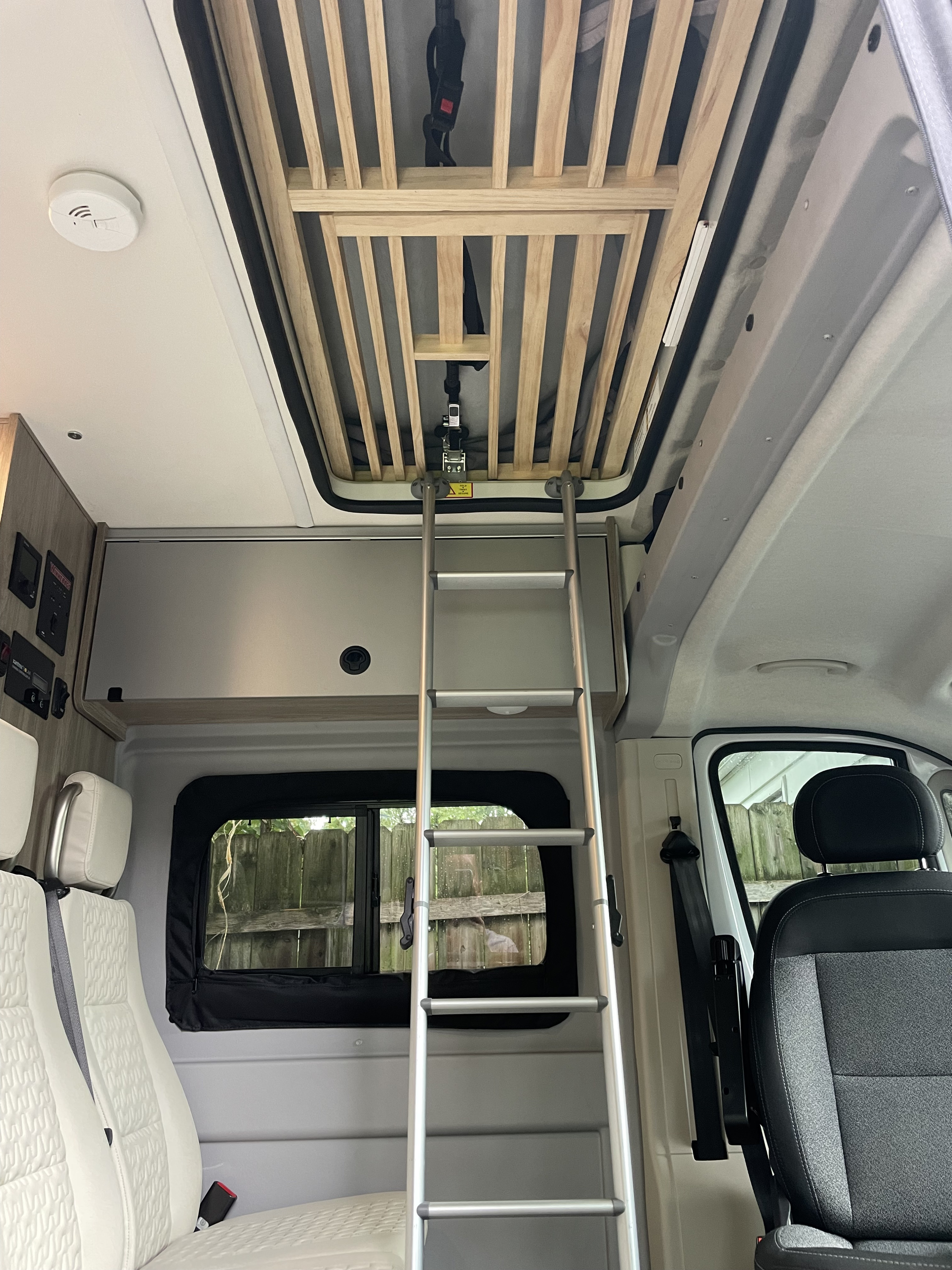 This RV rental interior features a cozy upper bunk bed with a ladder, comfortable seating, and essential controls.. Winnebago Solis 2021