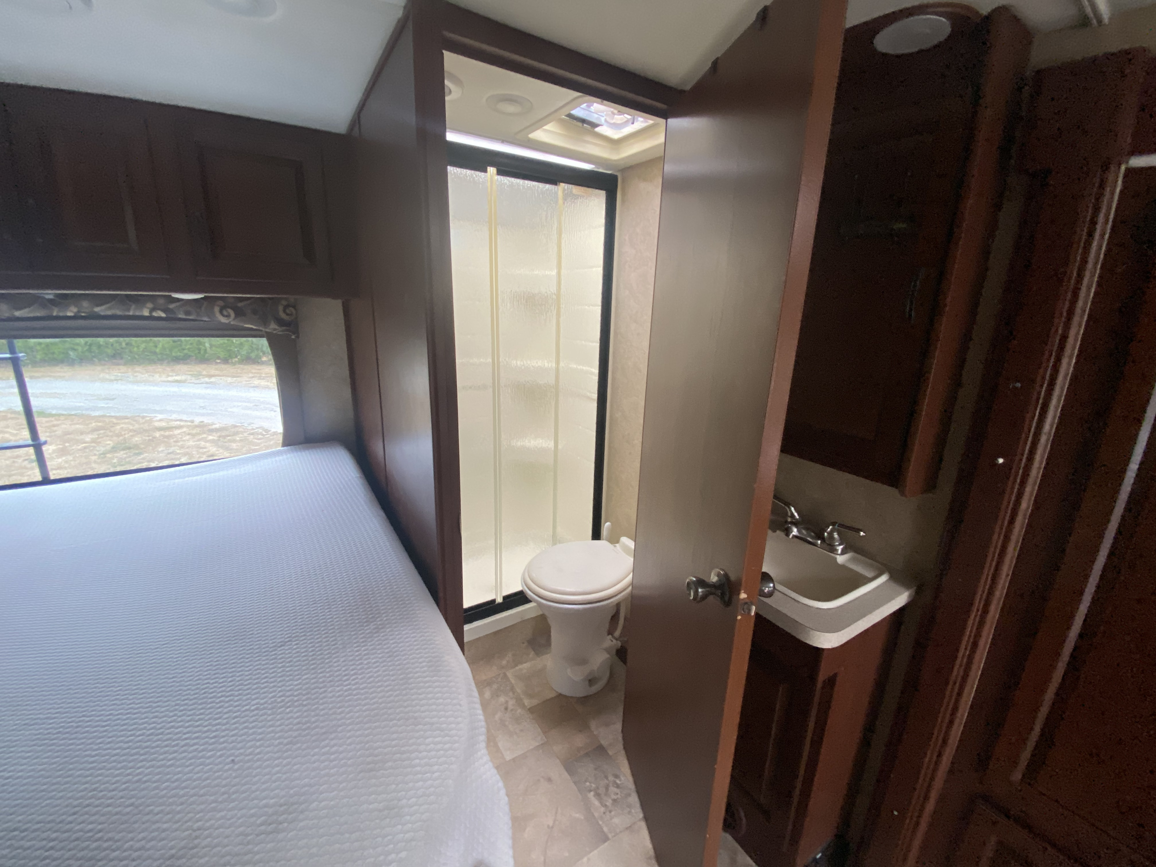 Inside an RV rental: view of a cozy bedroom area with a bed, and a compact bathroom featuring a toilet, shower, and sink.. Solera Solera Motorhome 2014