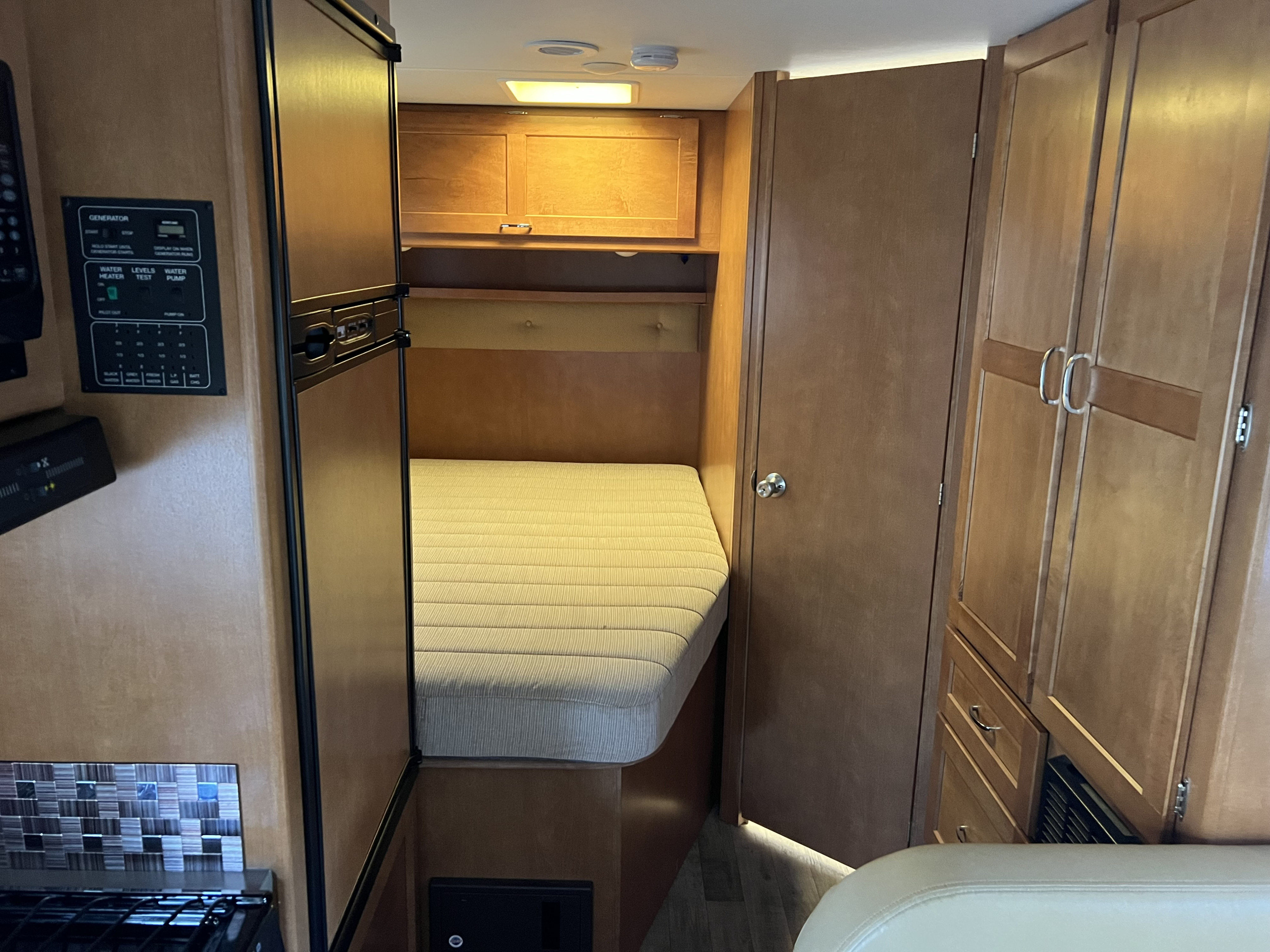 Step inside this RV rental, featuring a comfy bed, utility control panel, and wood cabinets, ready for adventure.. Winnebago Minnie Winnie 2018