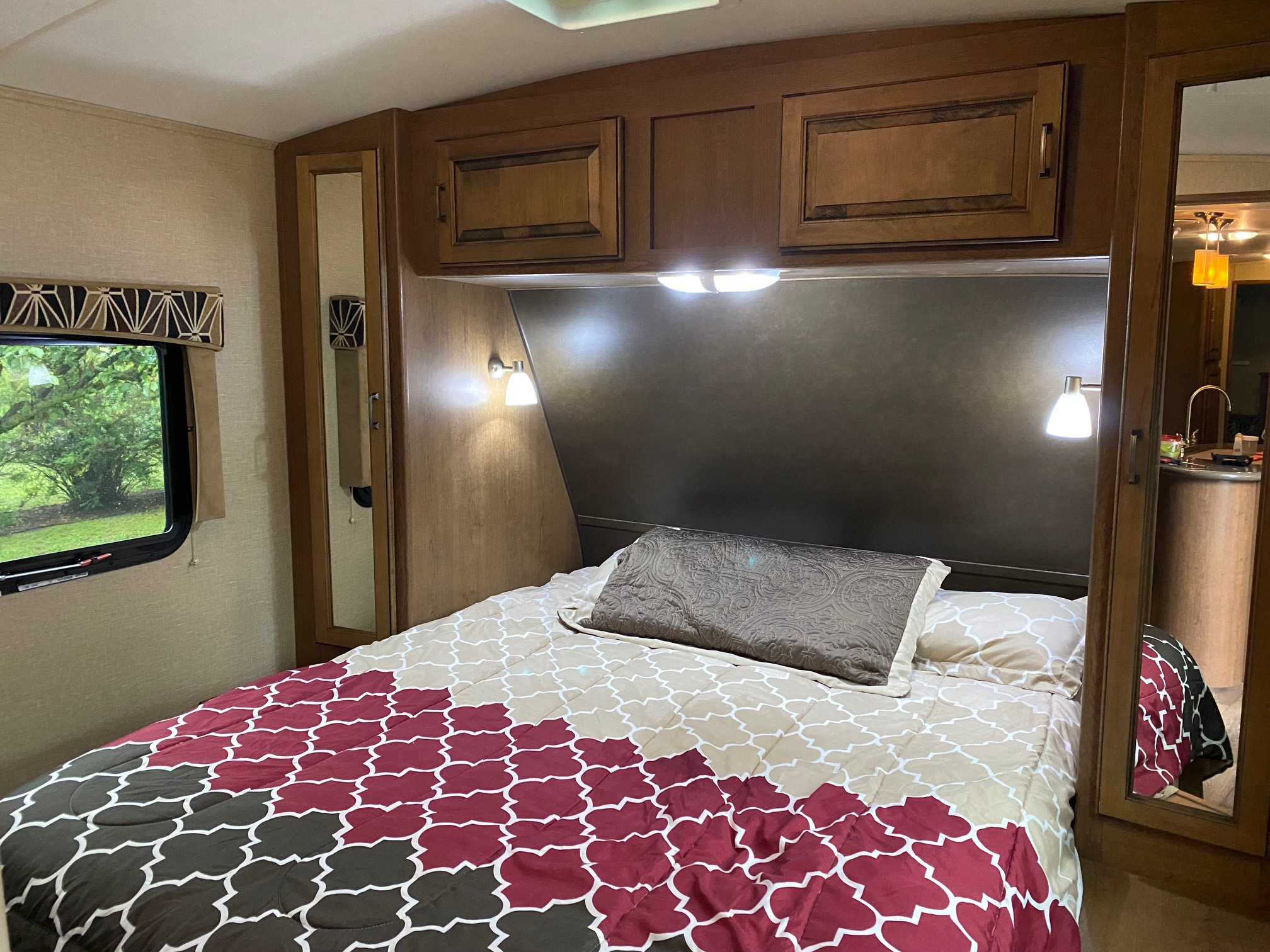 Cozy RV rental bedroom featuring a patterned bedspread, overhead cabinets, reading lights, and a window with a natural view.. Cruiser RV Fun Finder 2014
