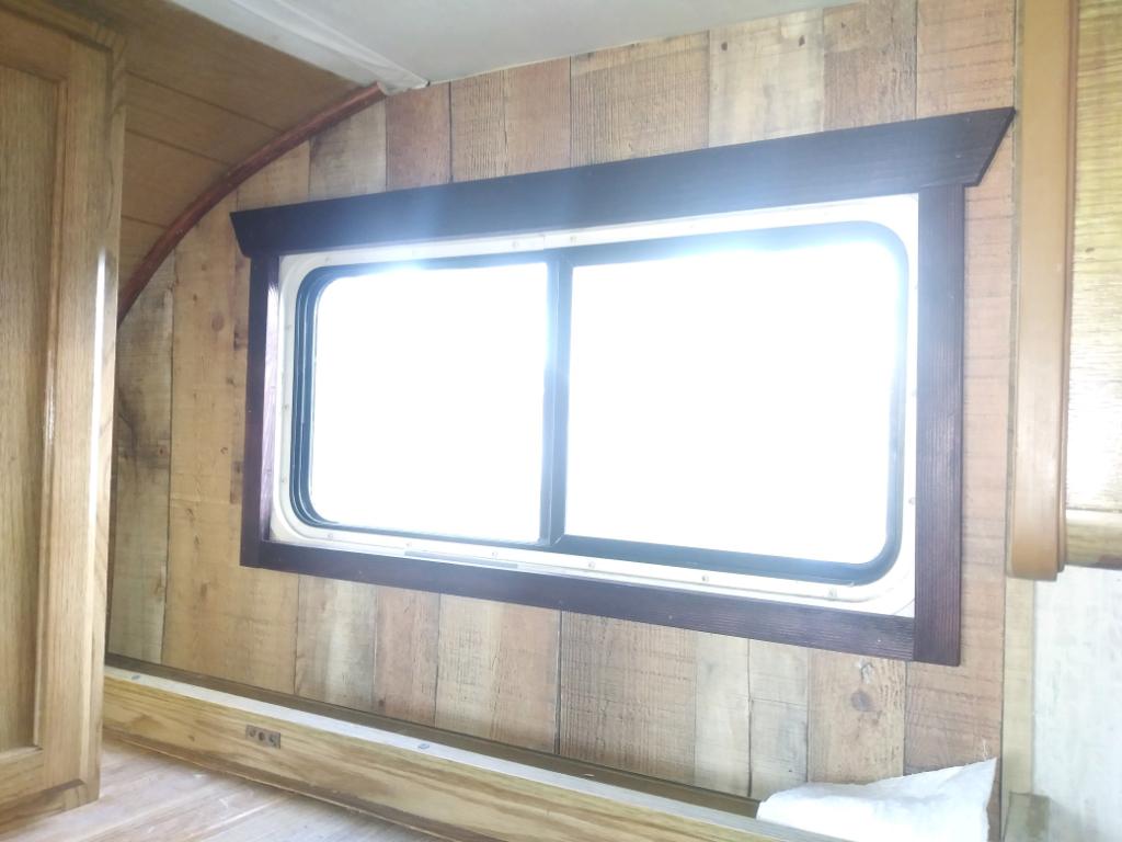 Inside an RV rental, a bright framed window against rustic wood paneling. Light wood cabinets and bed base complete the cozy interior.. Ford Tioga Montara 1992
