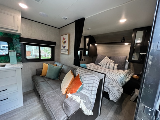 Cozy RV rental interior shows a modern living space with a couch, a bed, and a compact kitchen area.. Jayco Jay Flight SLX 2022