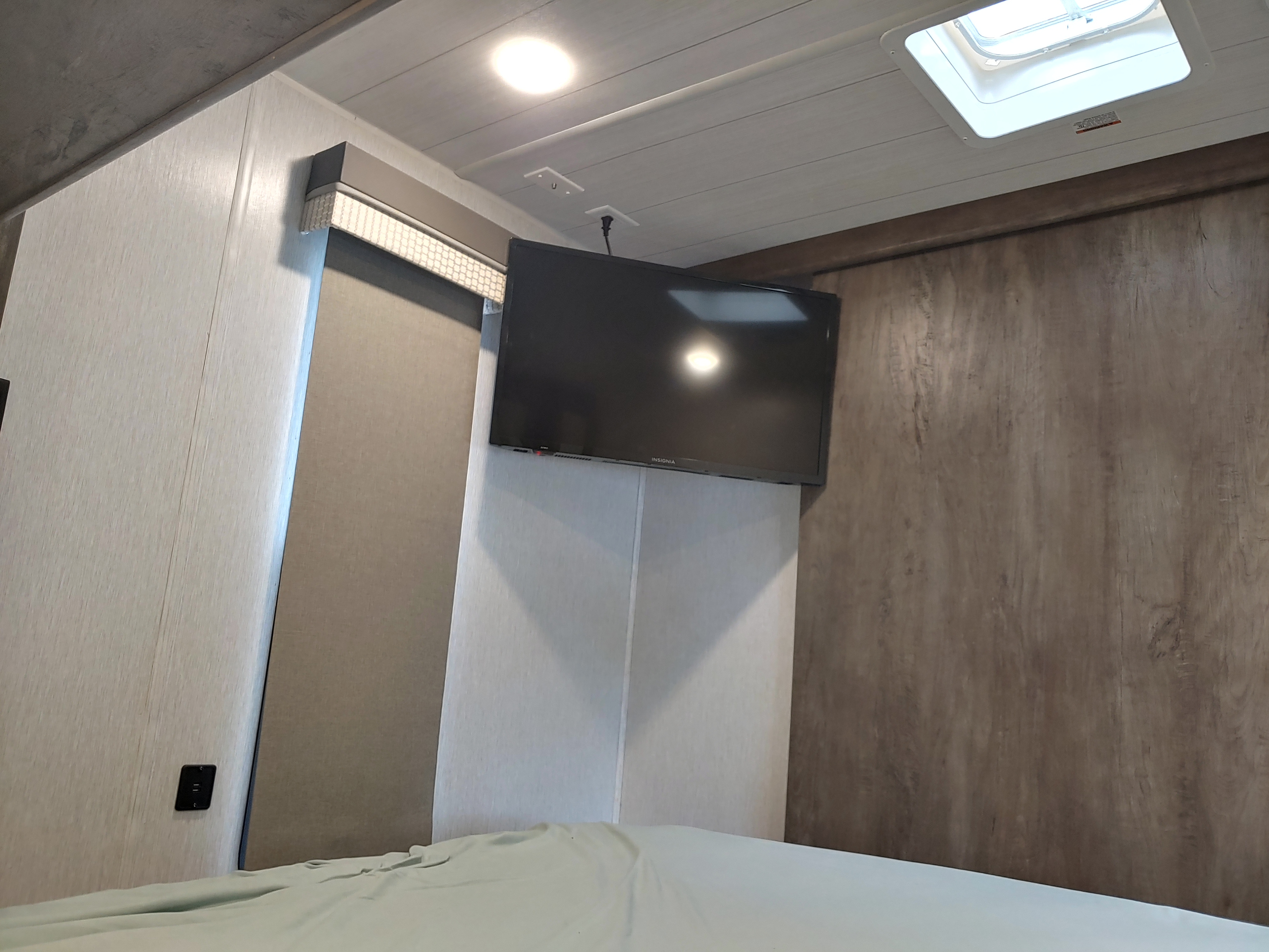 Cozy RV rental bedroom with a wall-mounted TV, light ceiling, and skylight above a made bed.. Forest River Wildwood 2022