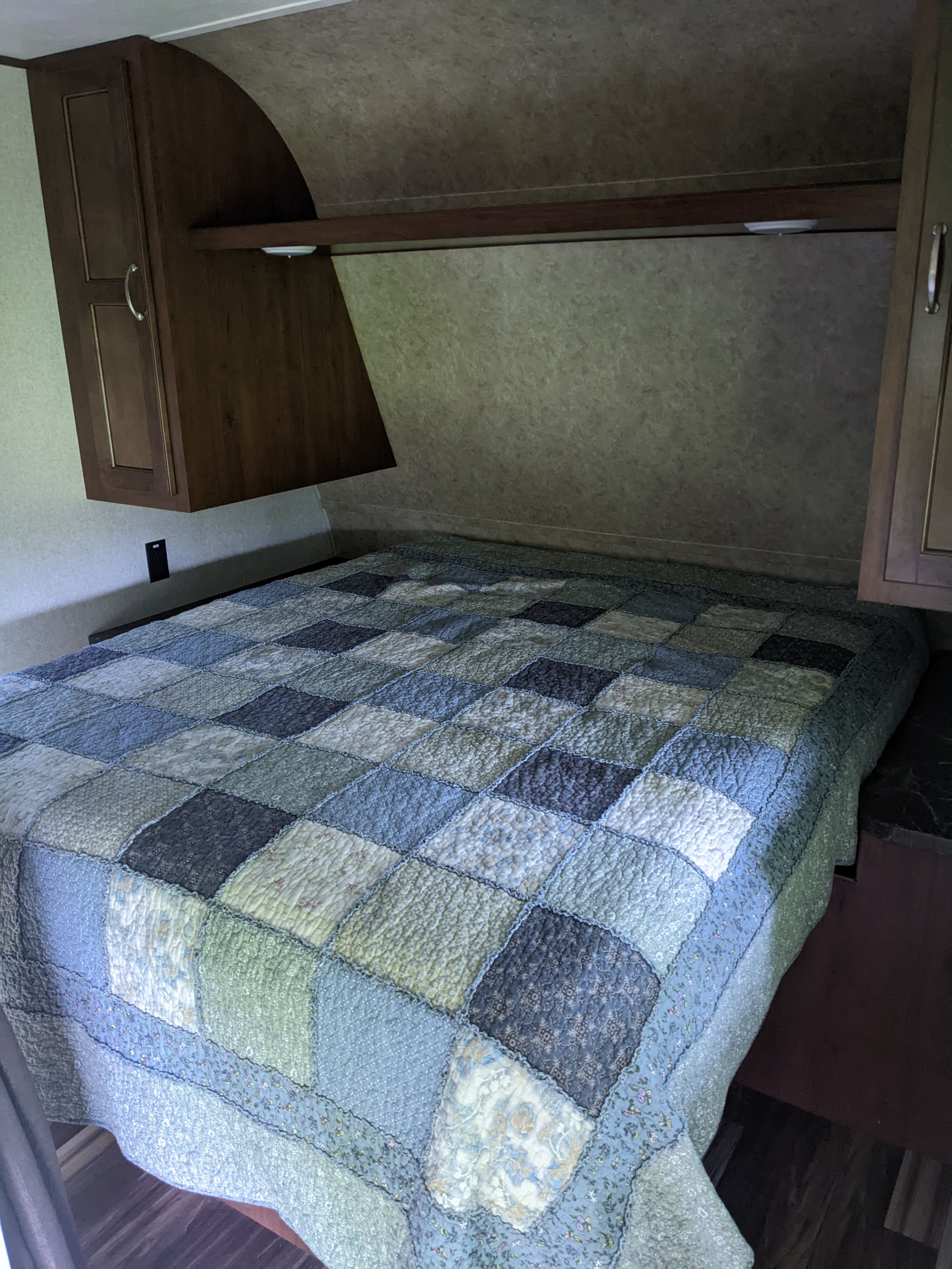 RV rental bedroom with a cozy patchwork quilt, overhead cabinets, and a reading light above the bed.. Jayco Jay Flight 2017
