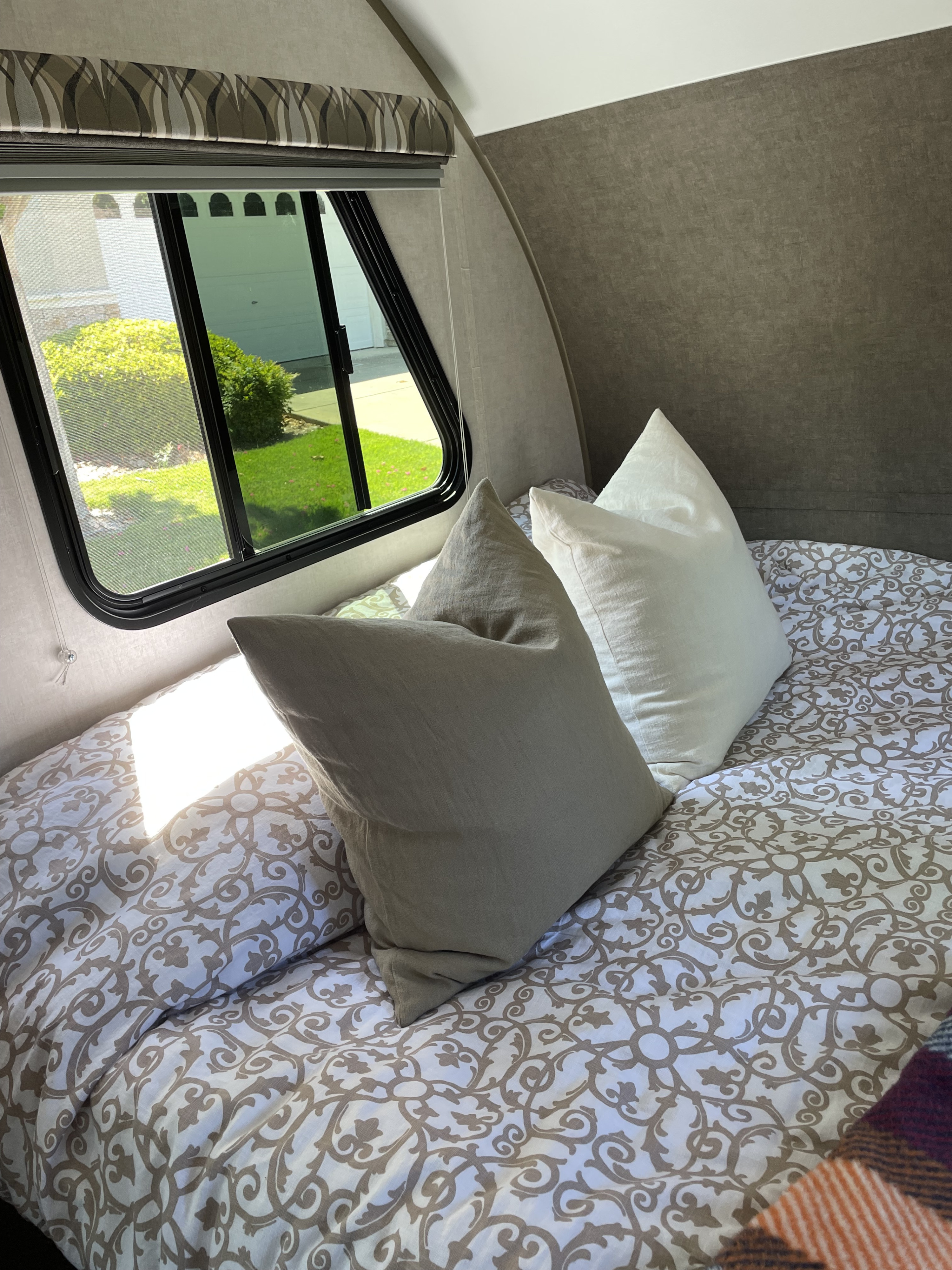 Bright RV rental bedroom features a patterned bed, soft pillows, and a large window overlooking a sunny yard.. R-Pod Hood River Edition 2017