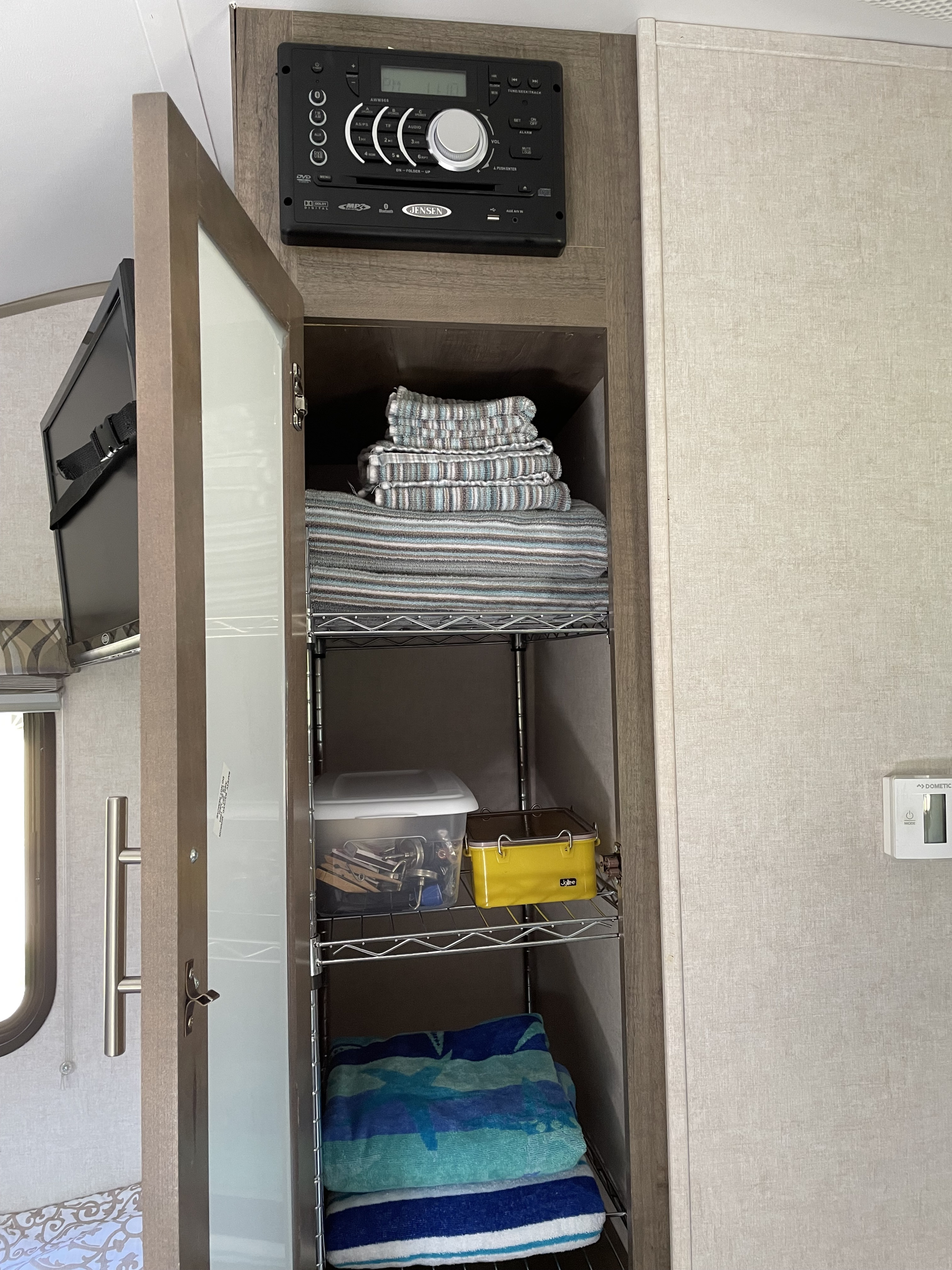 RV rental interior with open organized cabinet, showing towels, bins, a Jensen stereo, and a Dometic thermostat.. R-Pod Hood River Edition 2017