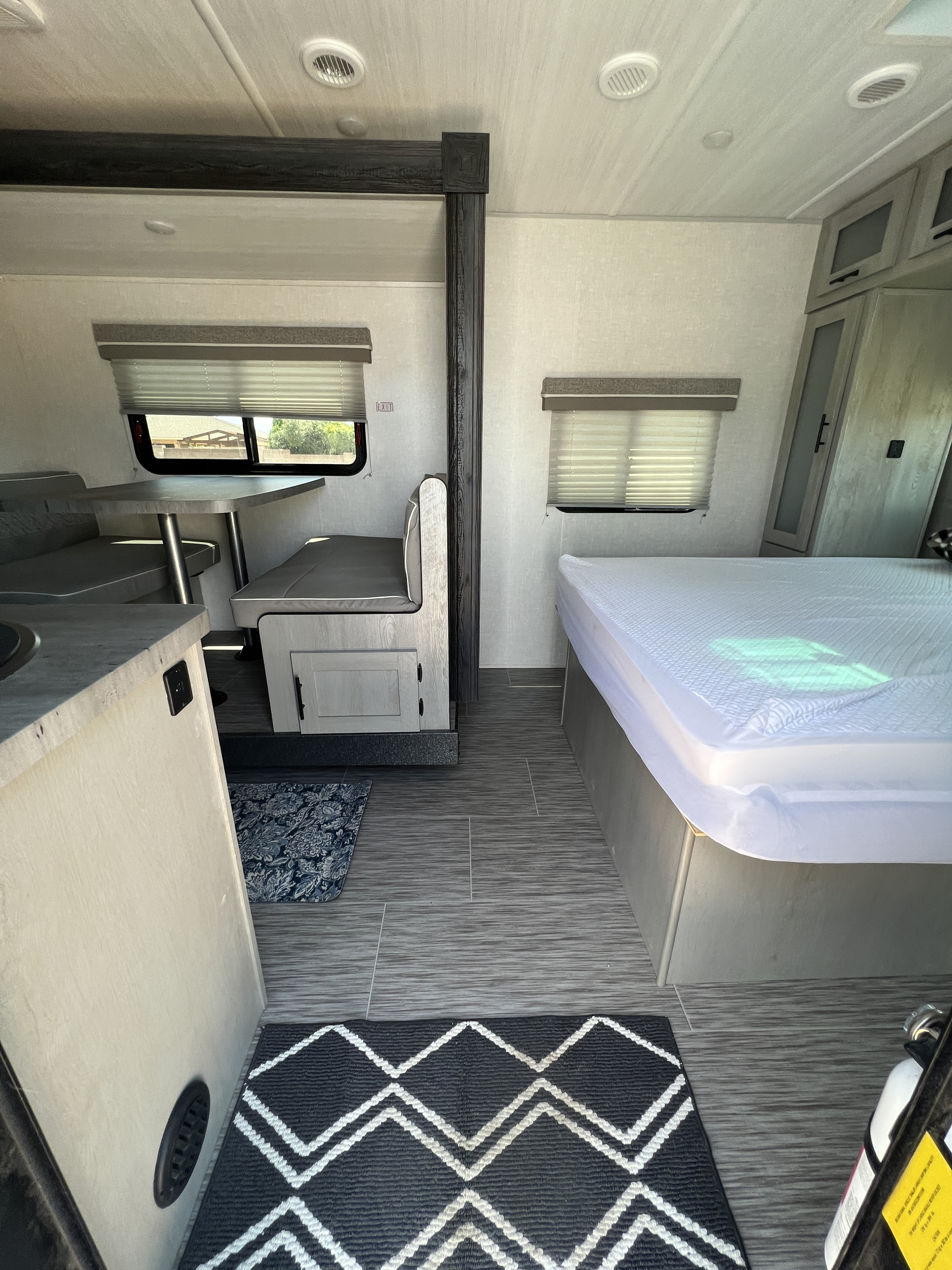 Inside a modern RV rental: a spacious dinette, compact kitchen counter, and a comfortable bed. Features grey flooring and light walls.. Forest River IBEX 20BHS 2022