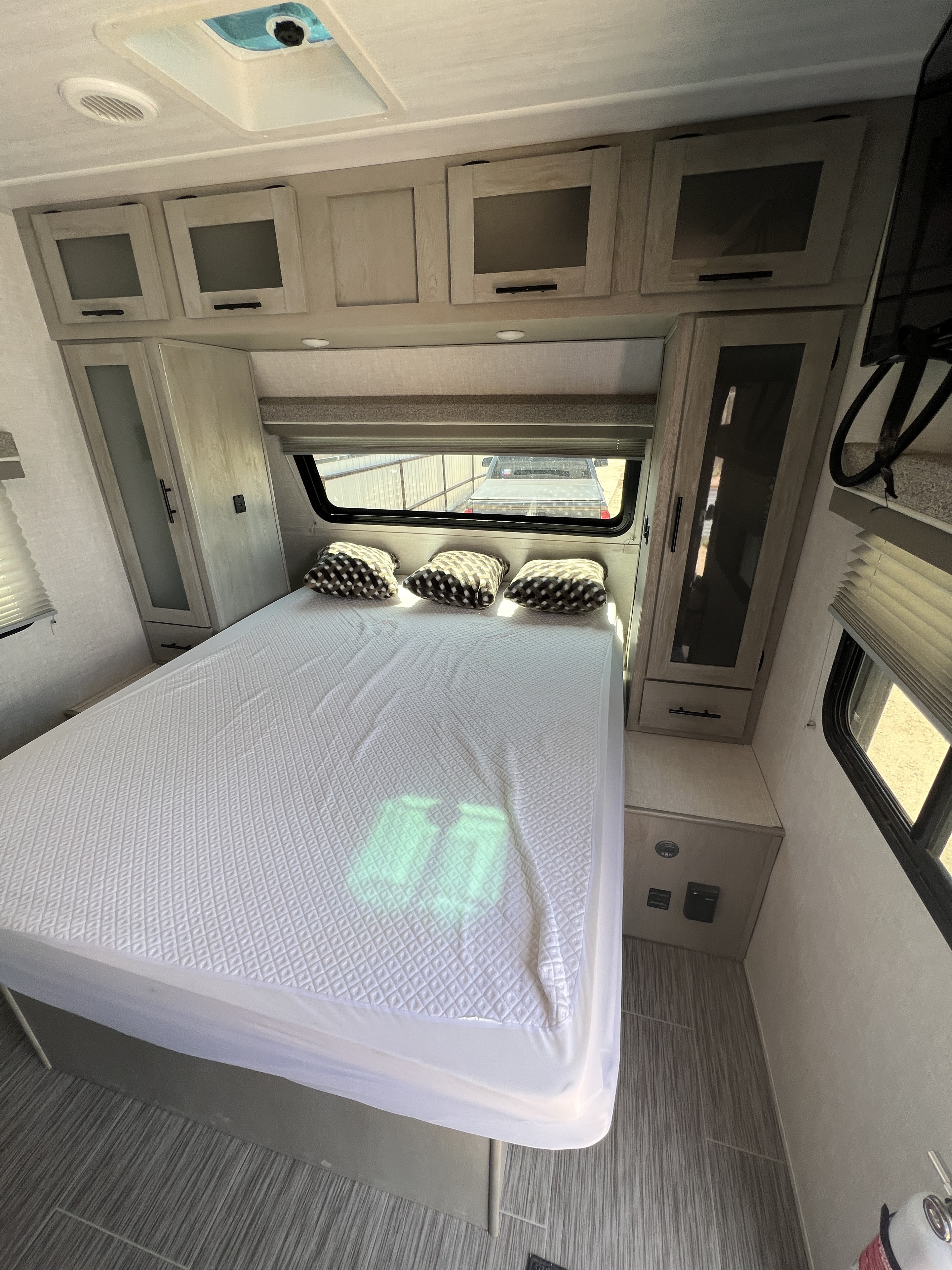 Inside an RV rental, a well-appointed bedroom featuring a comfortable bed, overhead cabinets, and large window.. Forest River IBEX 20BHS 2022