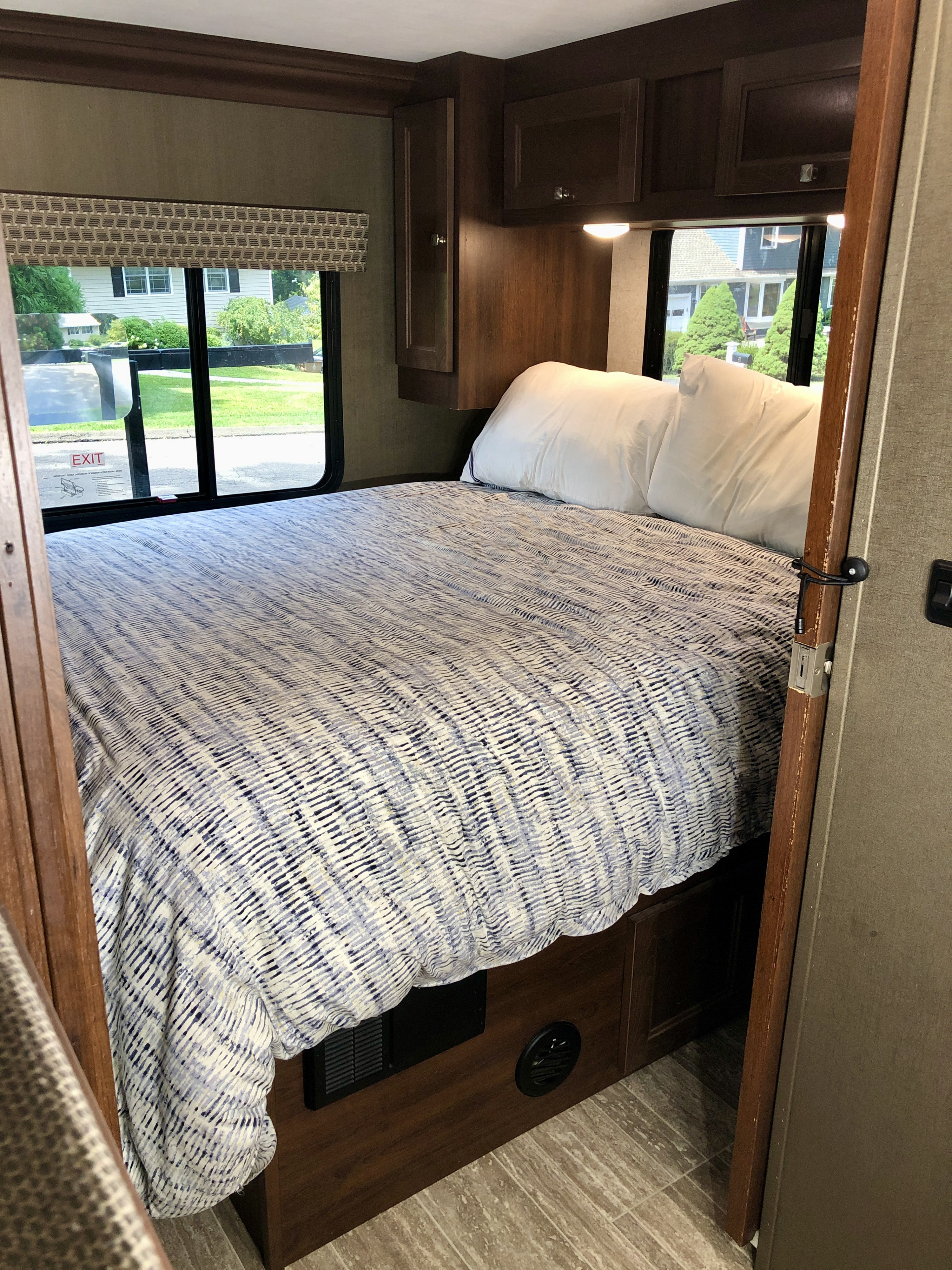 Cozy RV rental bedroom with a comfortable bed, large window, and wooden storage cabinets.. Forest River Sunseeker LE 2020