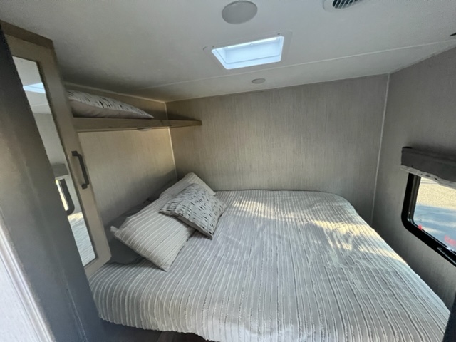 Cozy RV rental bedroom features a comfy bed with striped bedding, an overhead shelf, mirror, and window.. Forest River Palomino Puma 2022